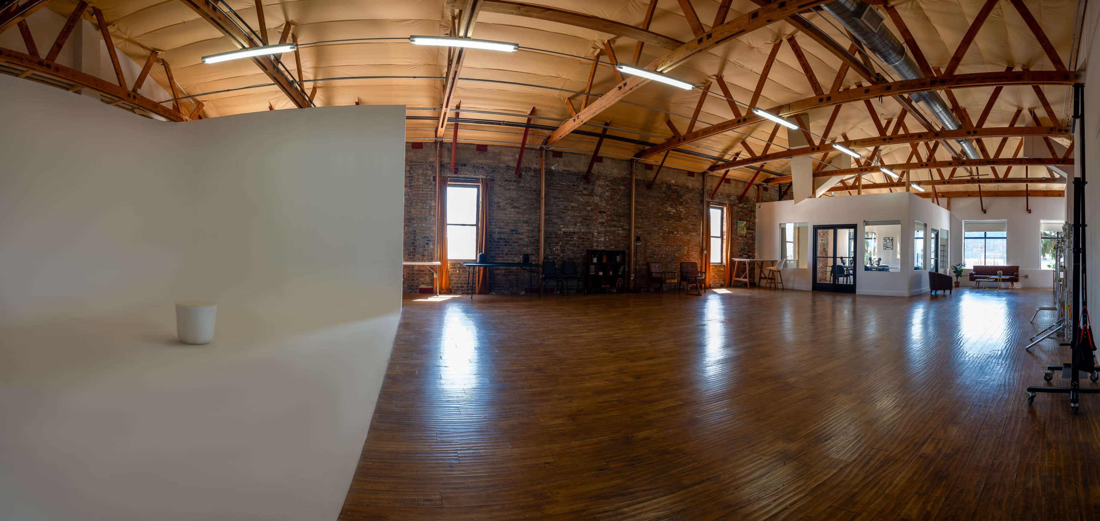 A spacious, well-lit studio with wooden floors, a plain backdrop, and a large window overlooking an office area.