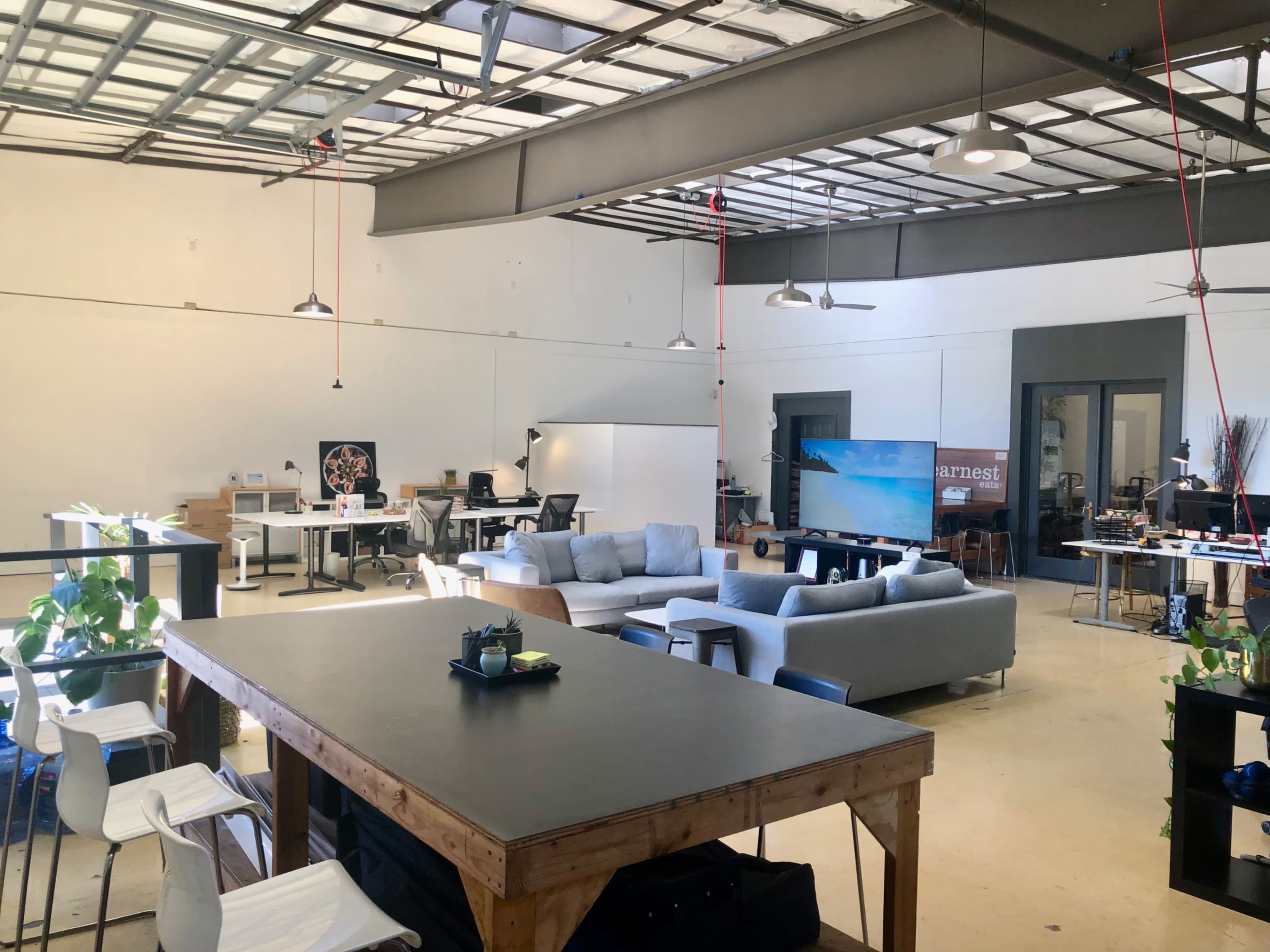 An open office space with multiple seating areas, workstations, and a large screen in a bright, minimalistic environment.