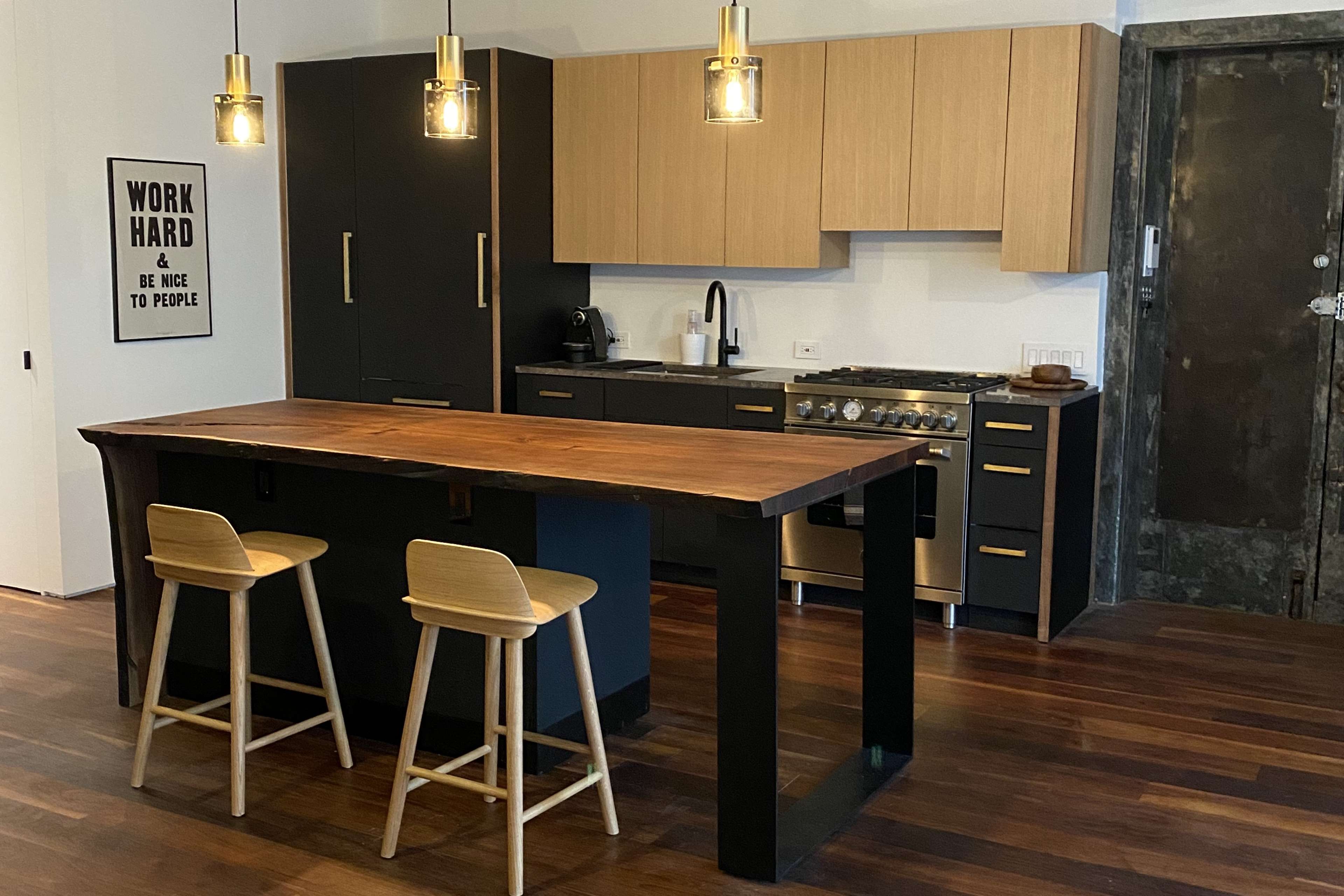 A modern kitchen featuring wooden cabinets, a large island with two stools, and stainless steel appliances.