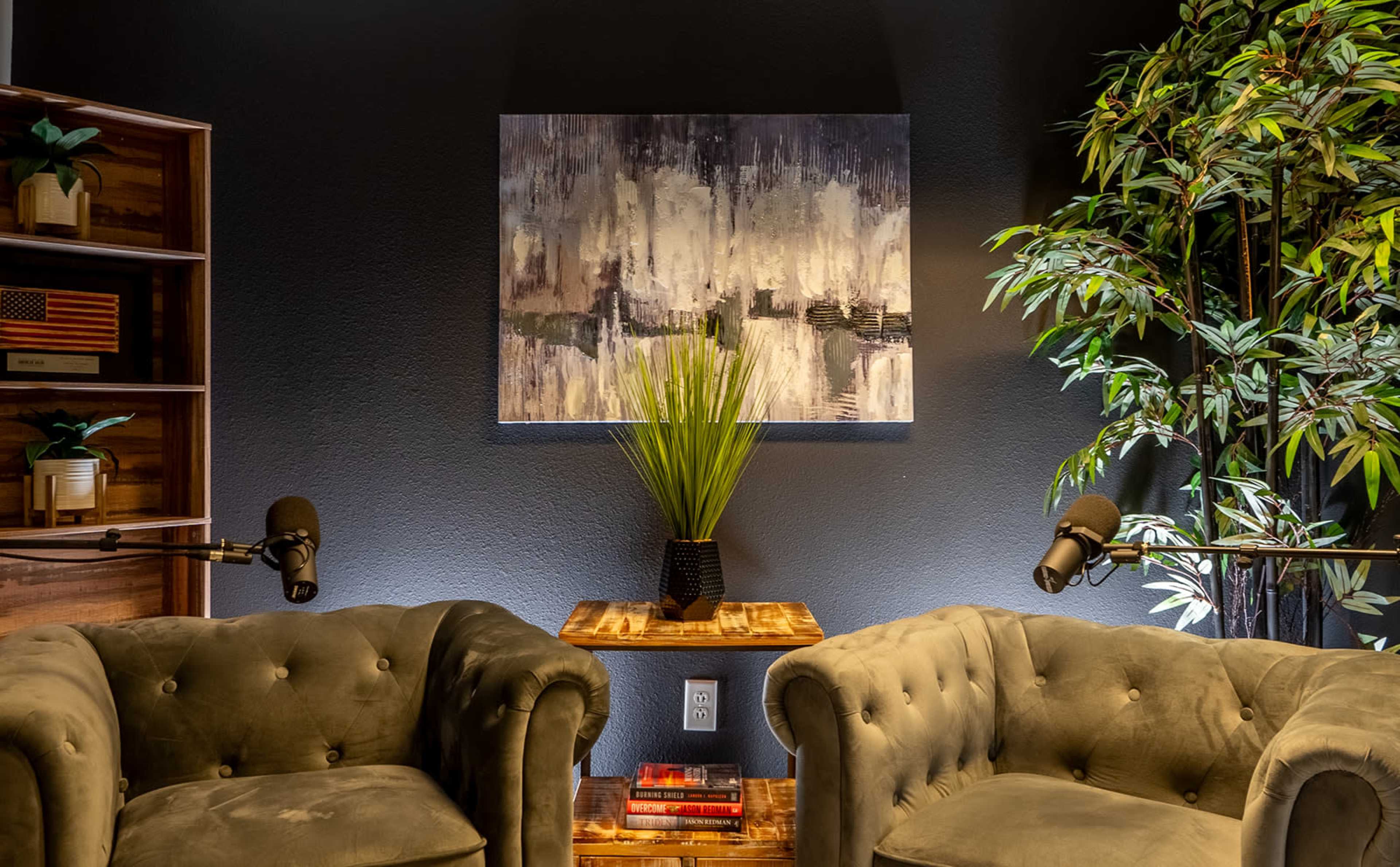 A cozy corner featuring two tufted armchairs, a small wooden table, a plant, and a piece of abstract artwork on the wall, all illuminated in soft lighting.