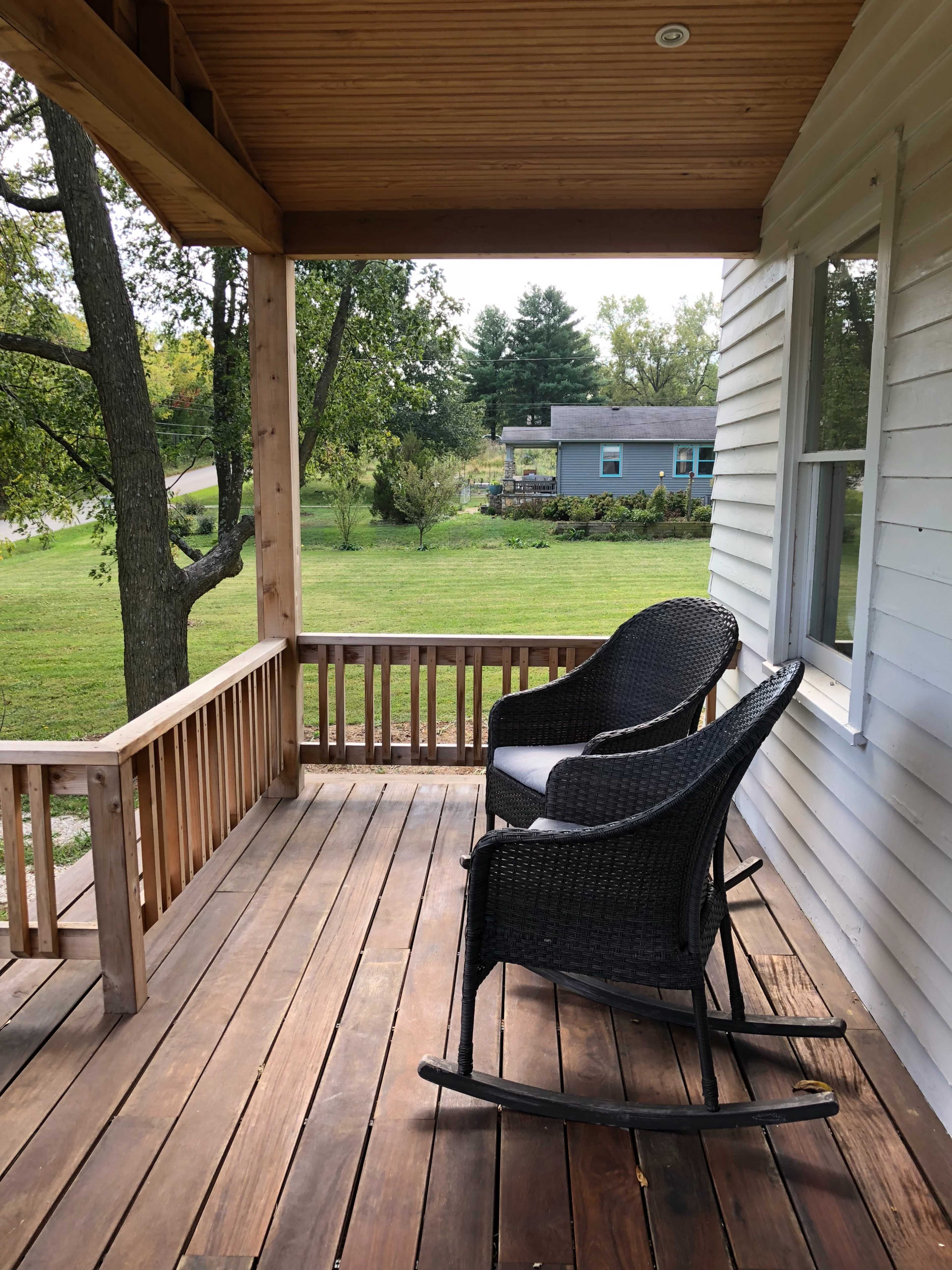 A porch features two rocking chairs overlooking a grassy yard and trees.