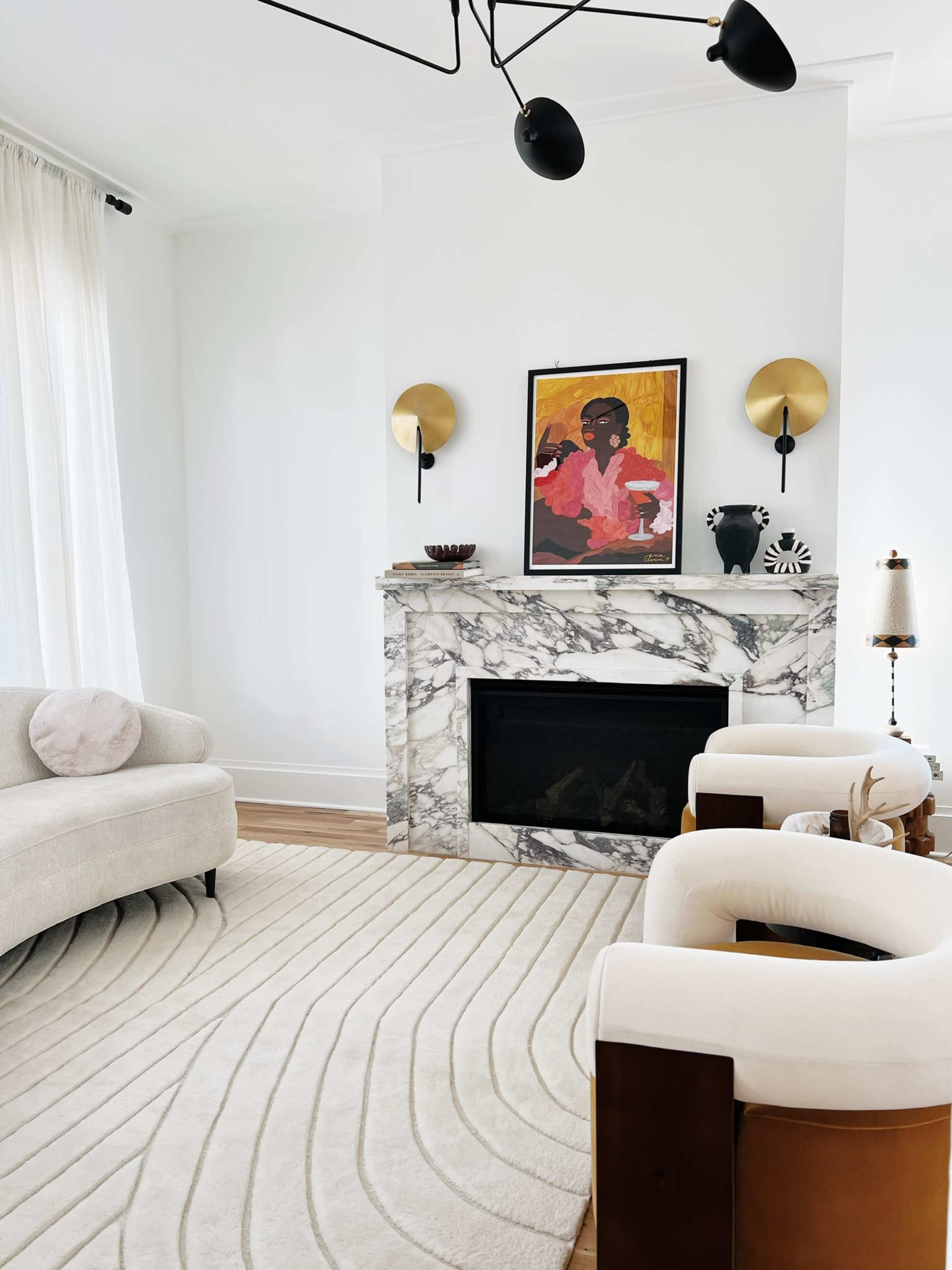 A modern living room featuring a marble fireplace, two upholstered chairs, a curved sofa, and a large area rug with a wavy design.