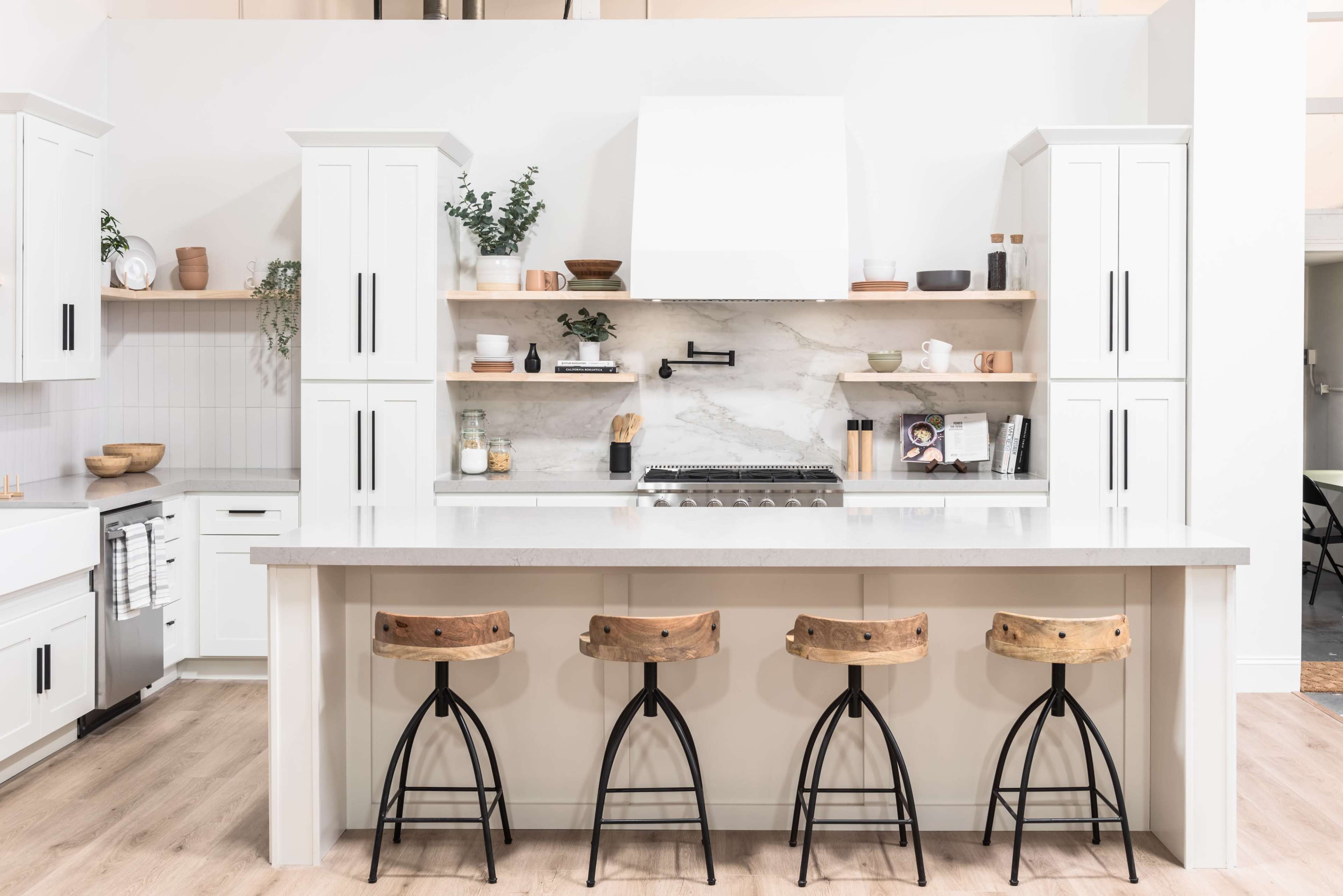 A modern kitchen with white cabinetry, a marble backsplash, and a central island featuring four wooden stools with black metal bases.