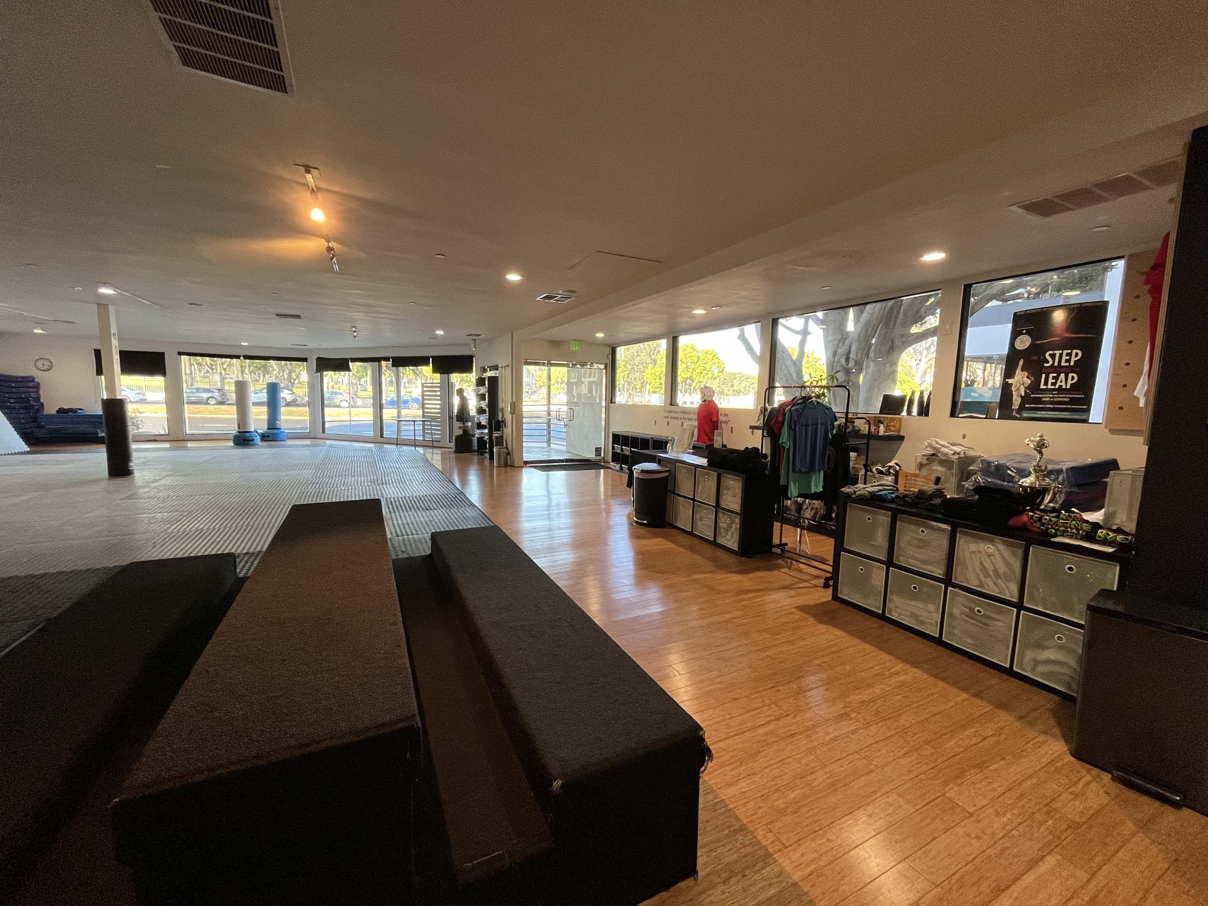 A spacious training facility with mats, benches, and merchandise displays visible near large windows.