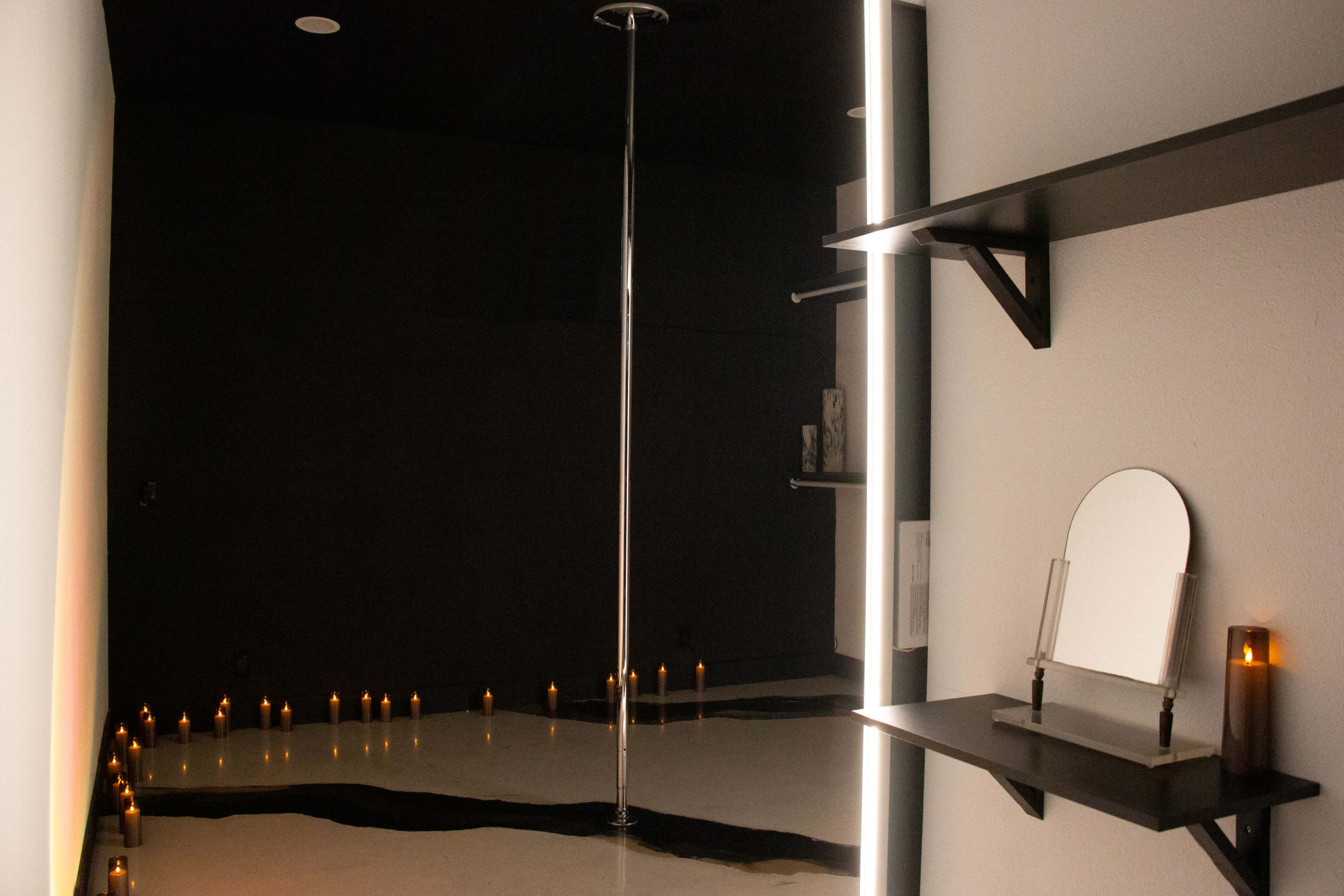 The image shows an interior room with a polished floor, a central pole, shelves with objects, and numerous candles arranged on the floor.