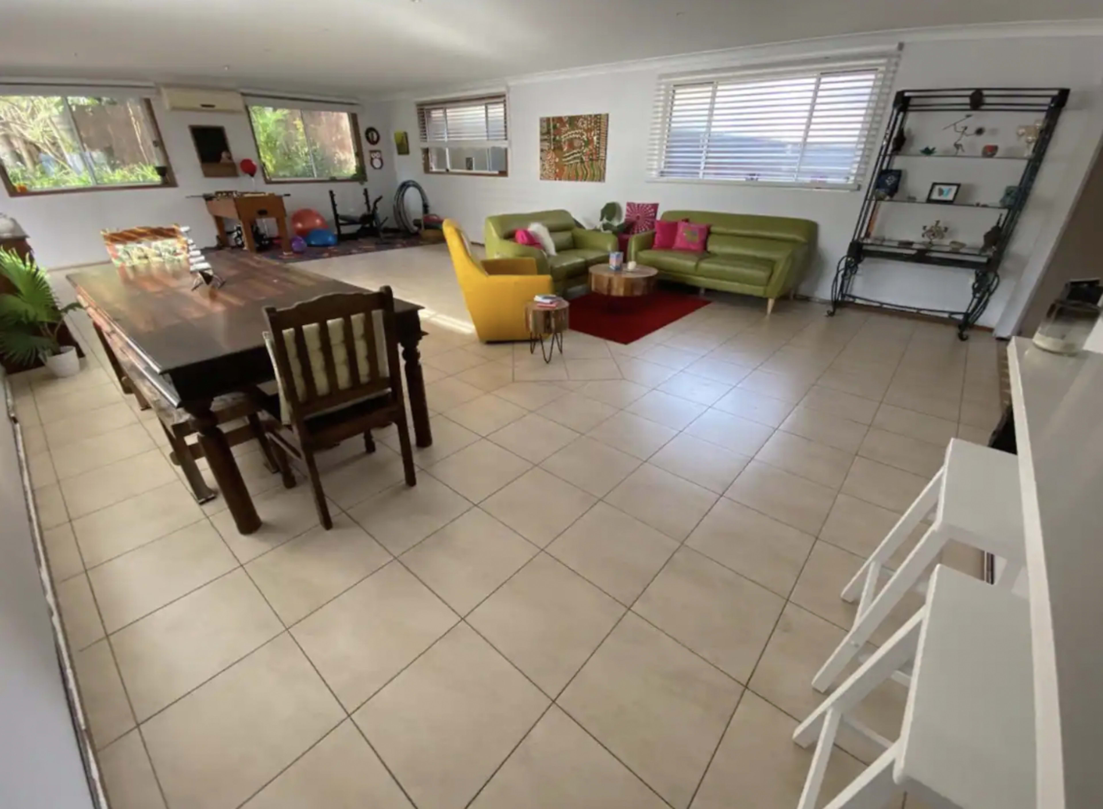 A spacious living area with a dining table, seating arrangements, and a collection of plants and decorations.
