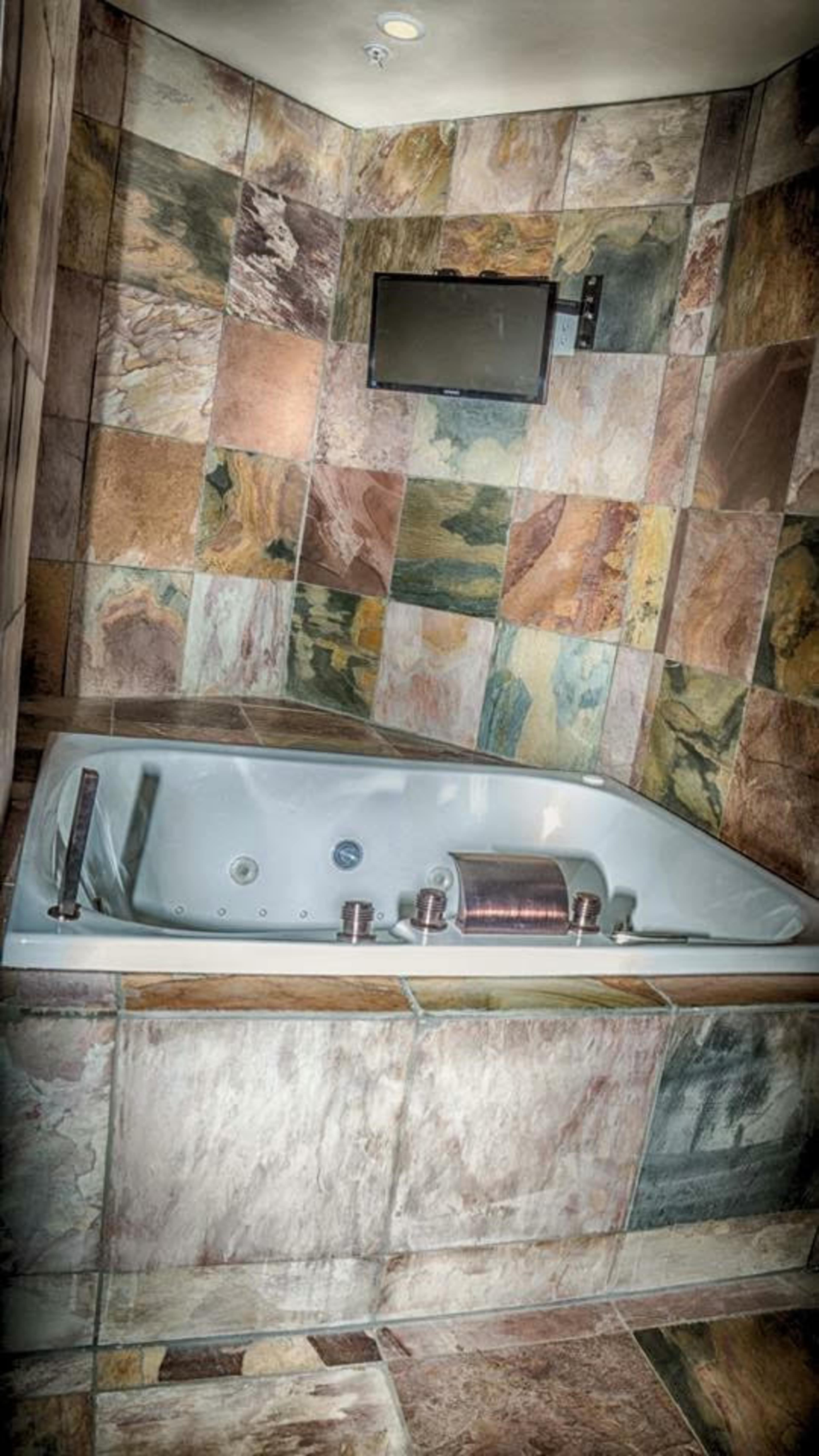 A modern bathroom featuring a large, white jacuzzi tub surrounded by colorful stone tiles and a wall-mounted television.