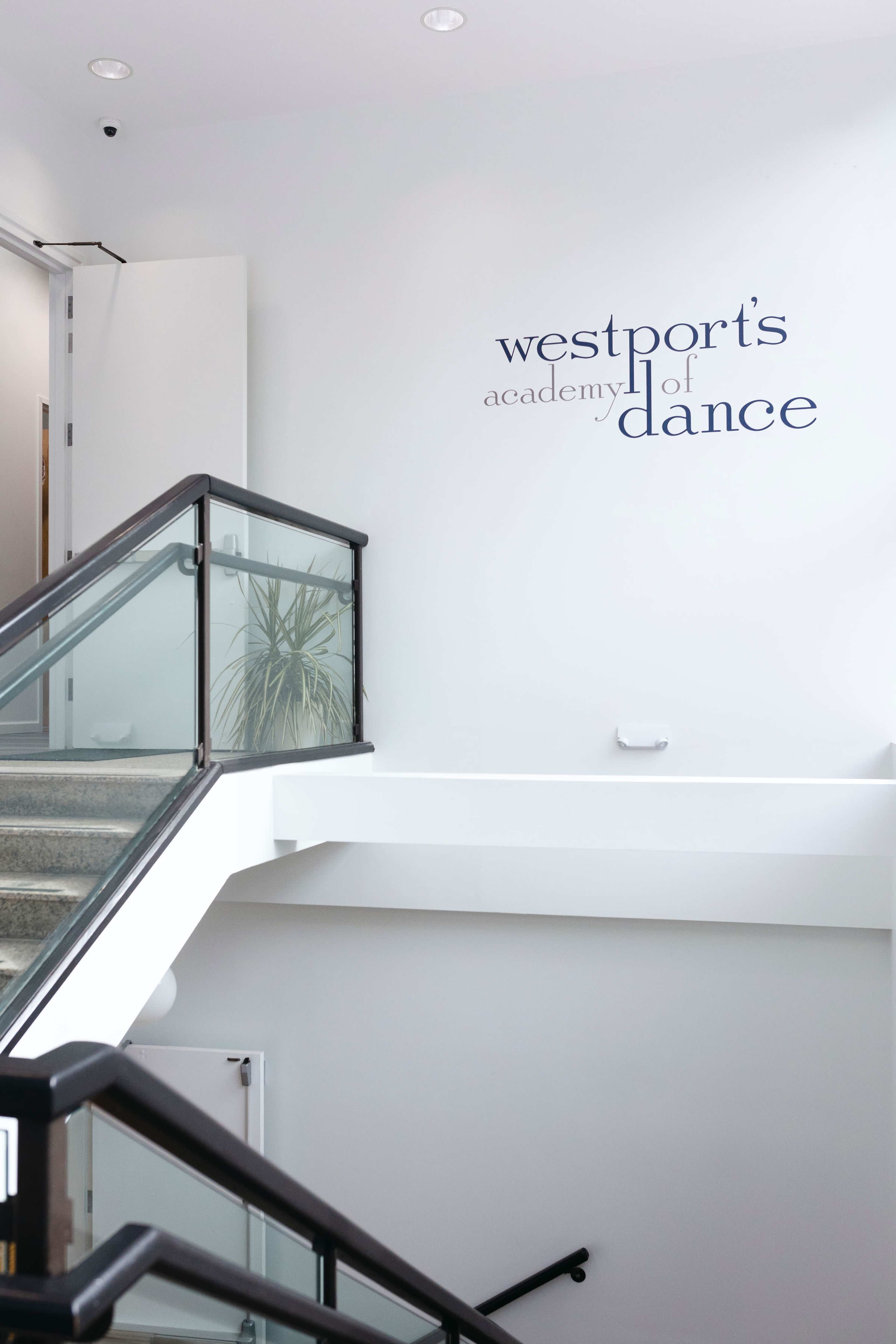 A stairway with a modern railing and a wall that displays the name "Westport's Academy of Dance."