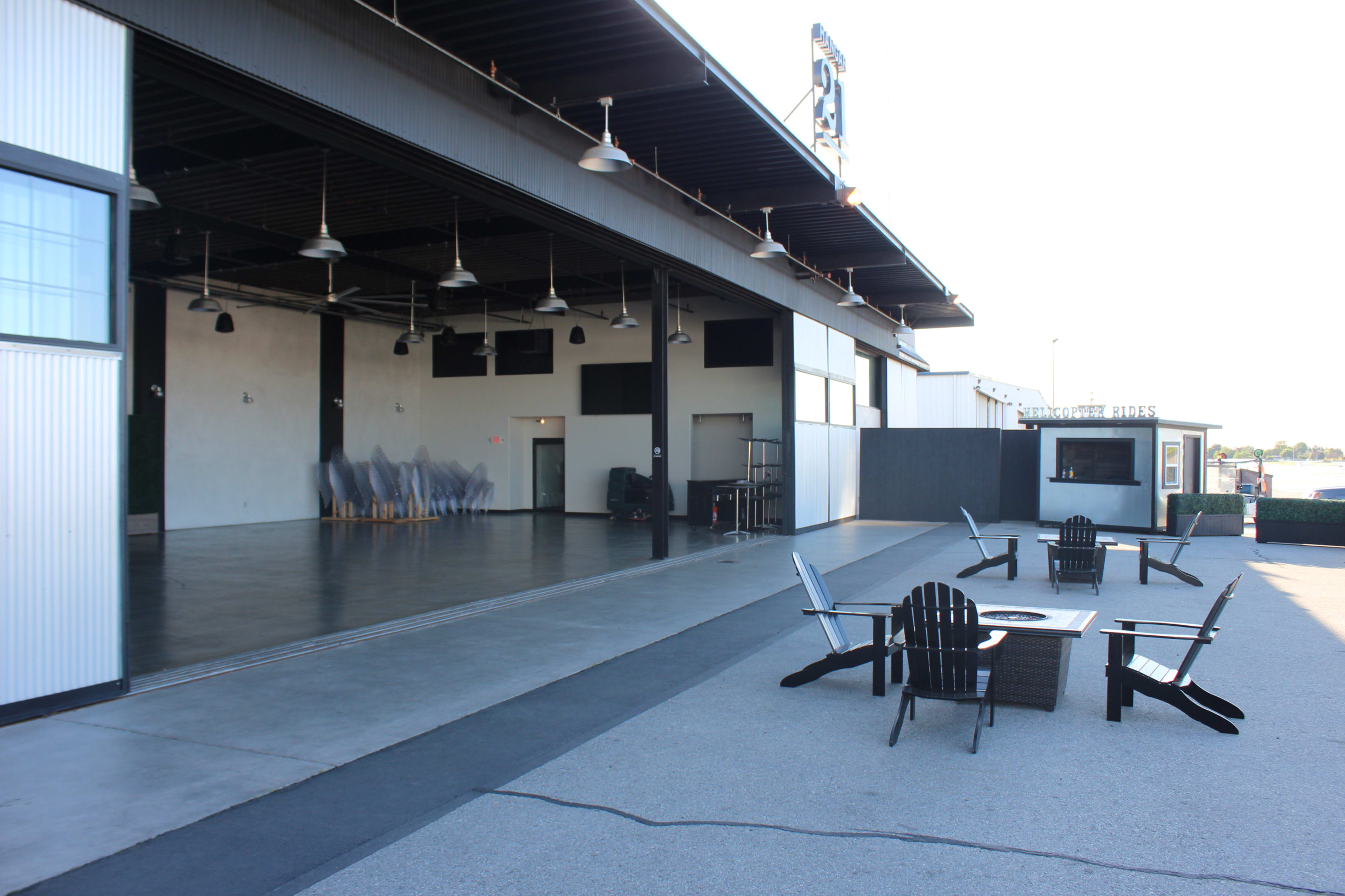 A large, open space with seating areas and a backdrop of a building featuring large glass doors, alongside a bar or service area nearby.