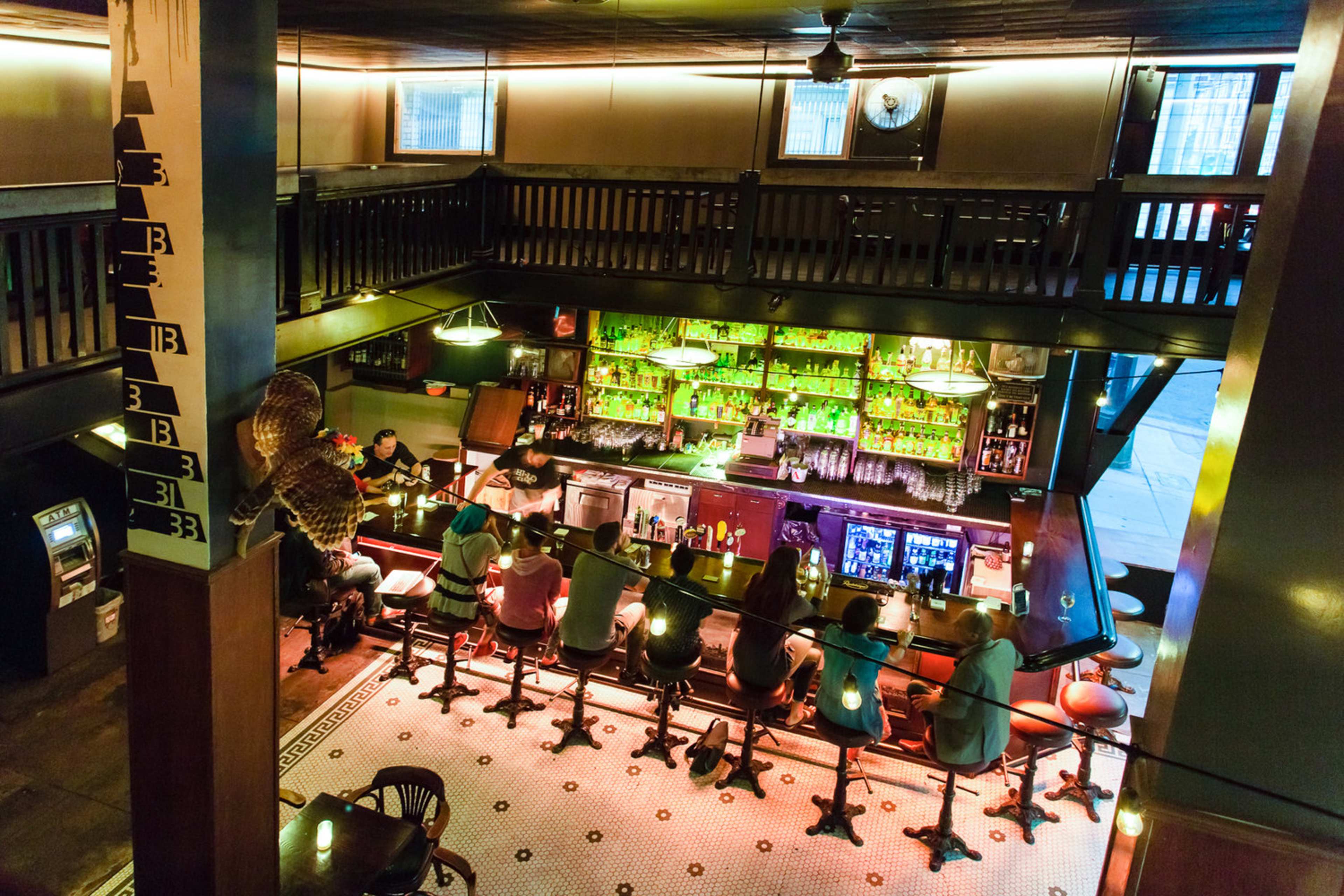 A vibrant bar scene with patrons seated at a counter, surrounded by illuminated shelves filled with various bottles.