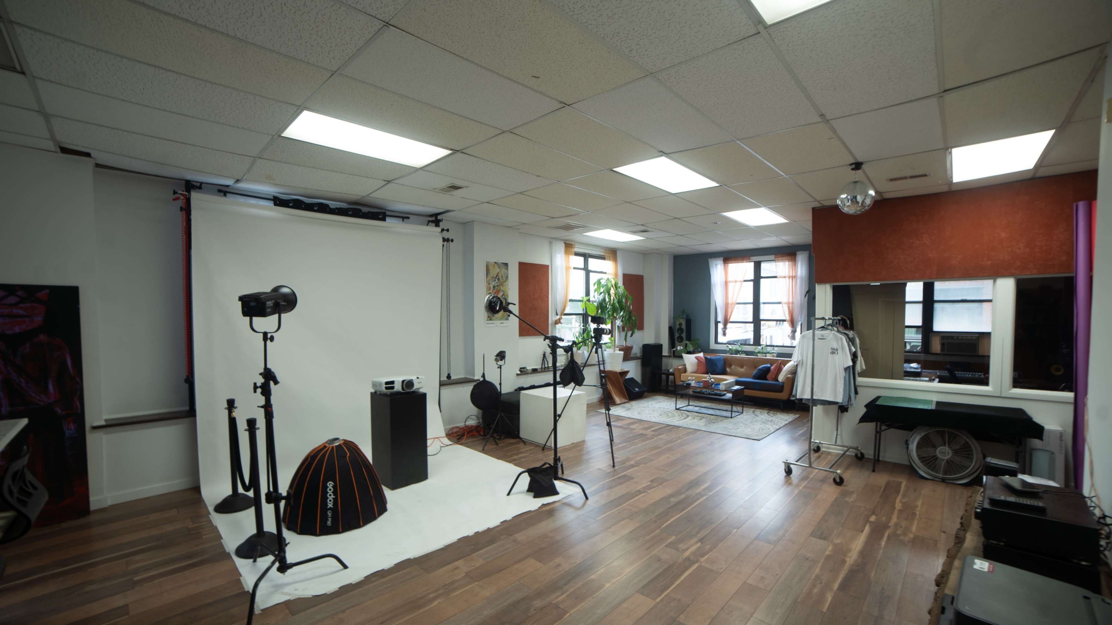 The image shows a spacious photography studio with various equipment, including lights and a backdrop, along with a lounge area featuring a sofa and decorative elements.