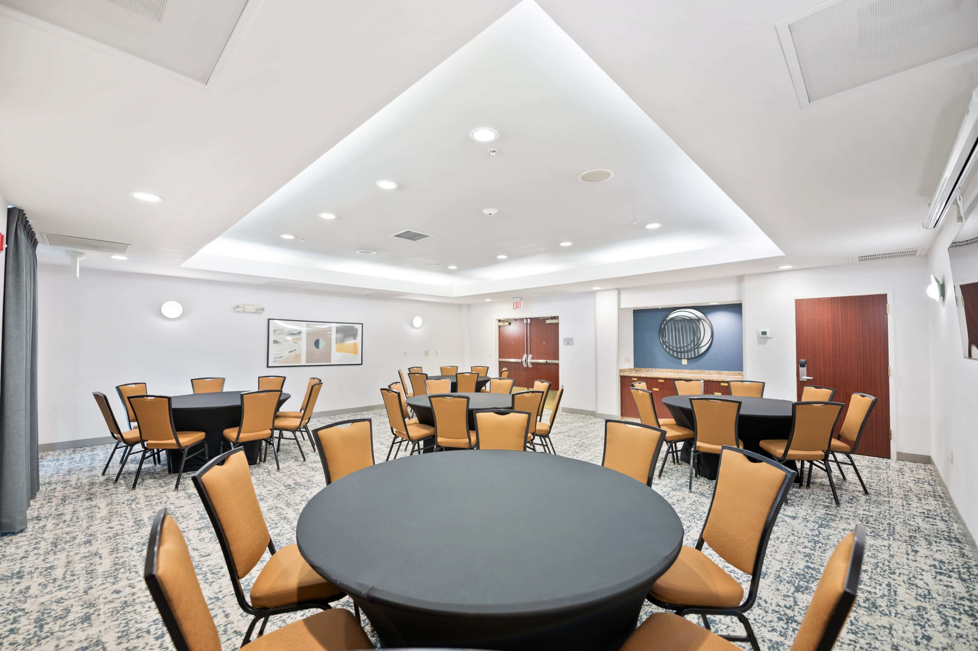 The image shows a well-lit meeting room with several round tables covered in black cloth and surrounded by brown chairs.