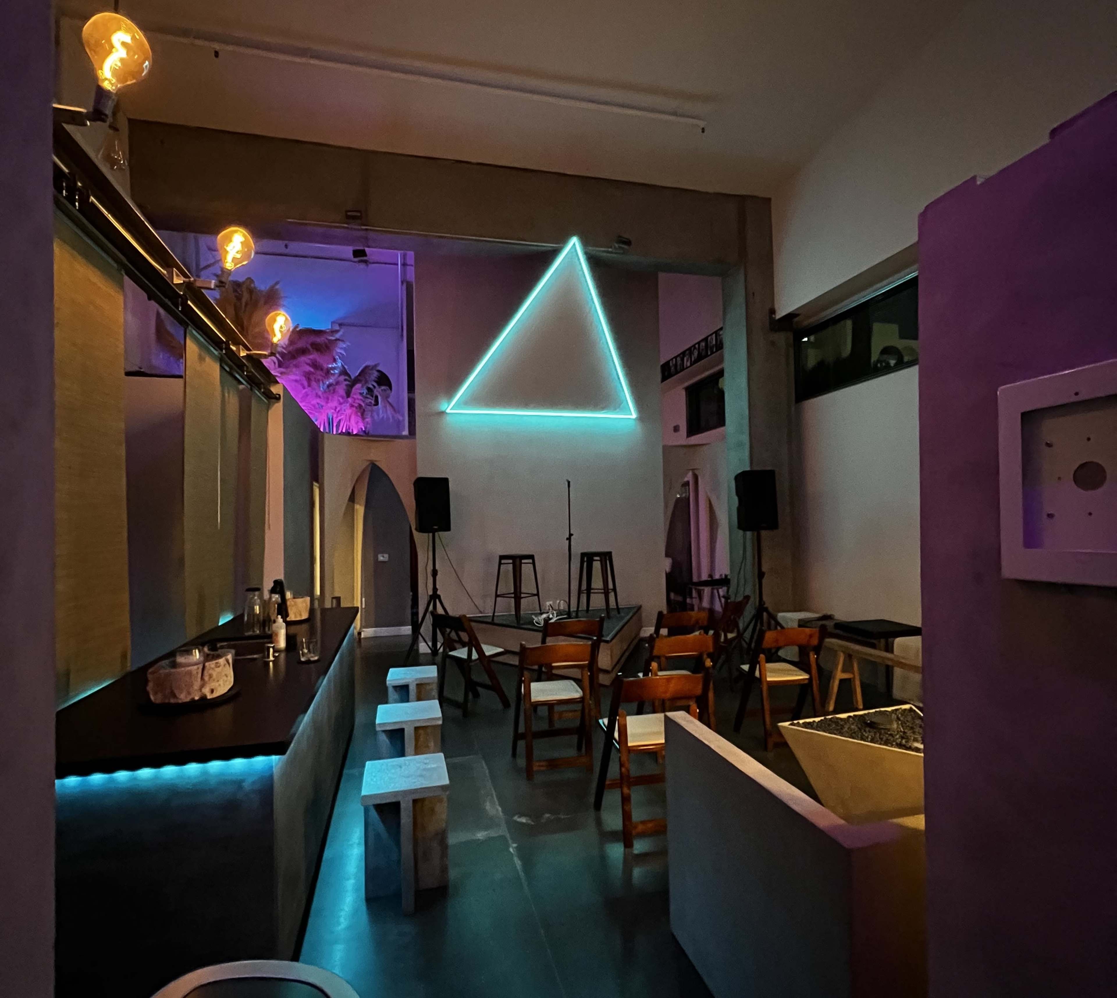 The image shows a modern interior space with a bar area and seating, highlighted by a large illuminated triangle on the wall and ambient lighting.
