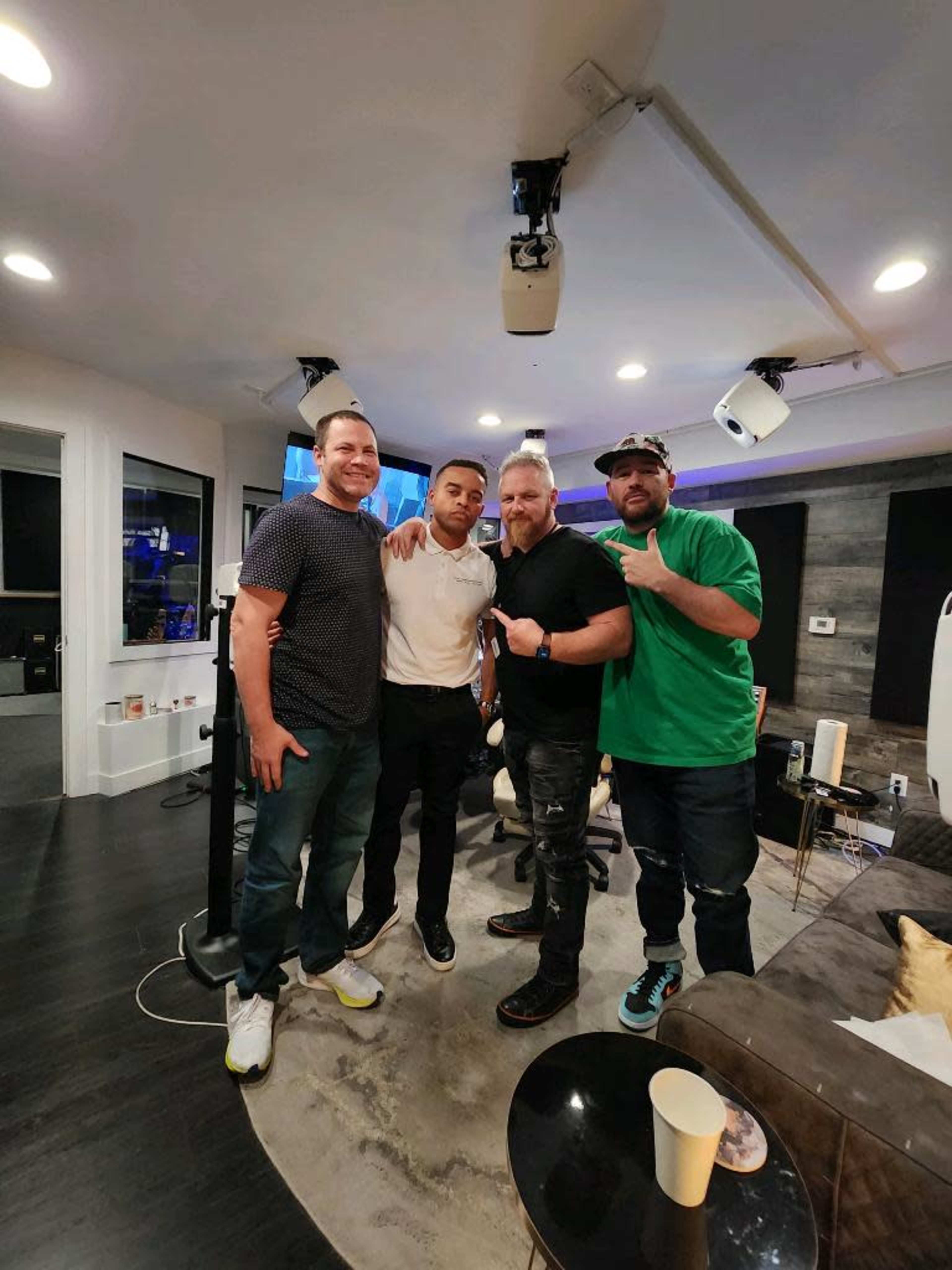 Four men pose together in a modern studio with a couch and various equipment in the background.
