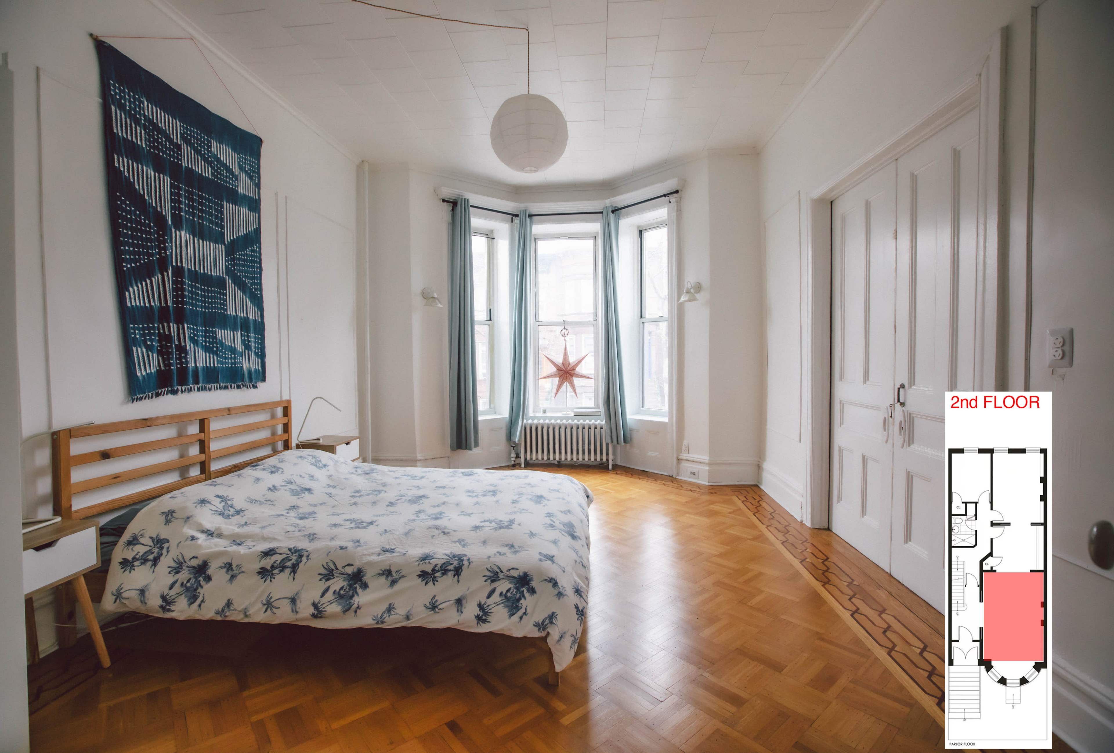 A spacious bedroom with a patterned bedspread, large windows, and a floor plan on the side.
