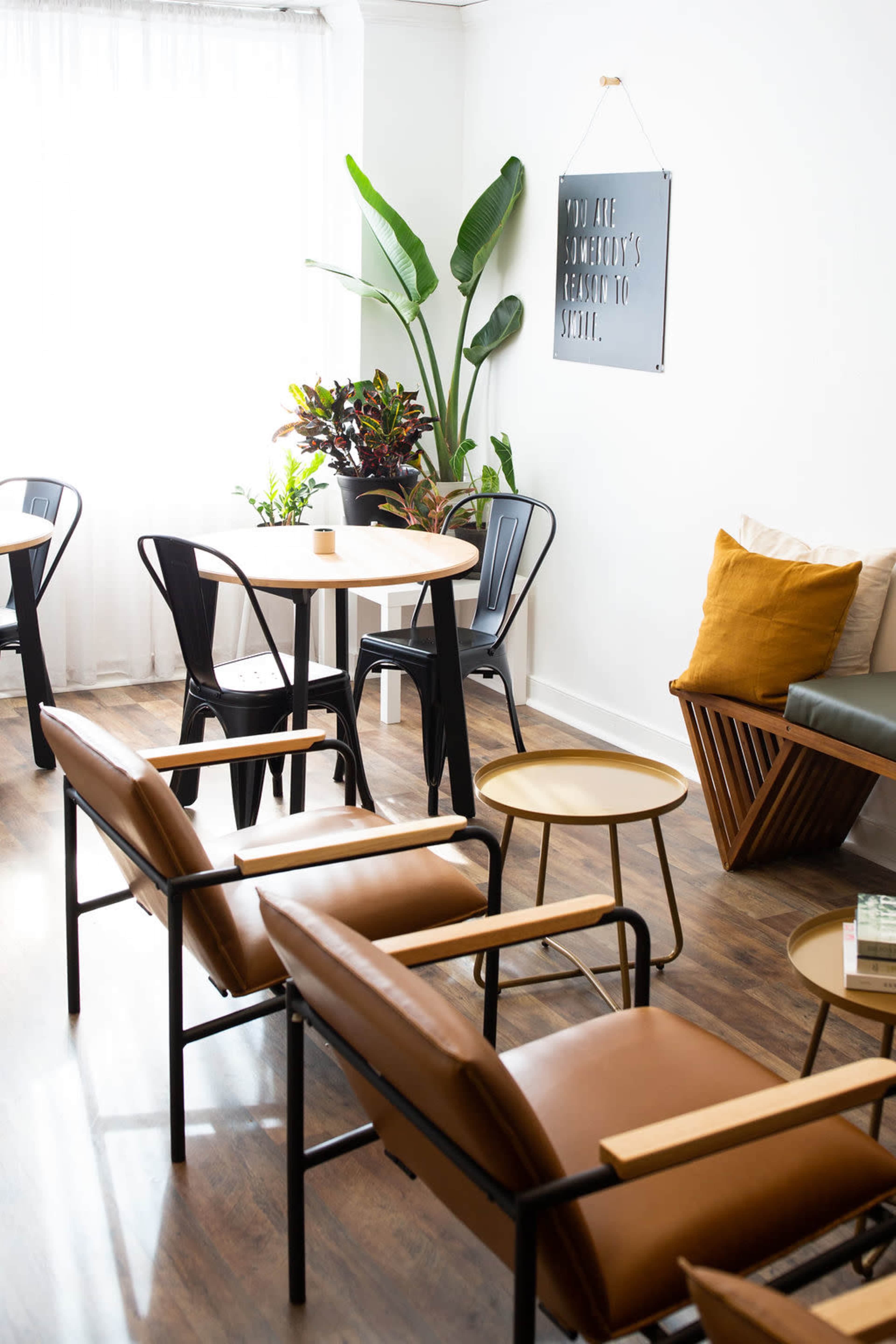 A bright, modern lounge area featuring stylish furniture, including leather chairs, a wooden table, and potted plants.