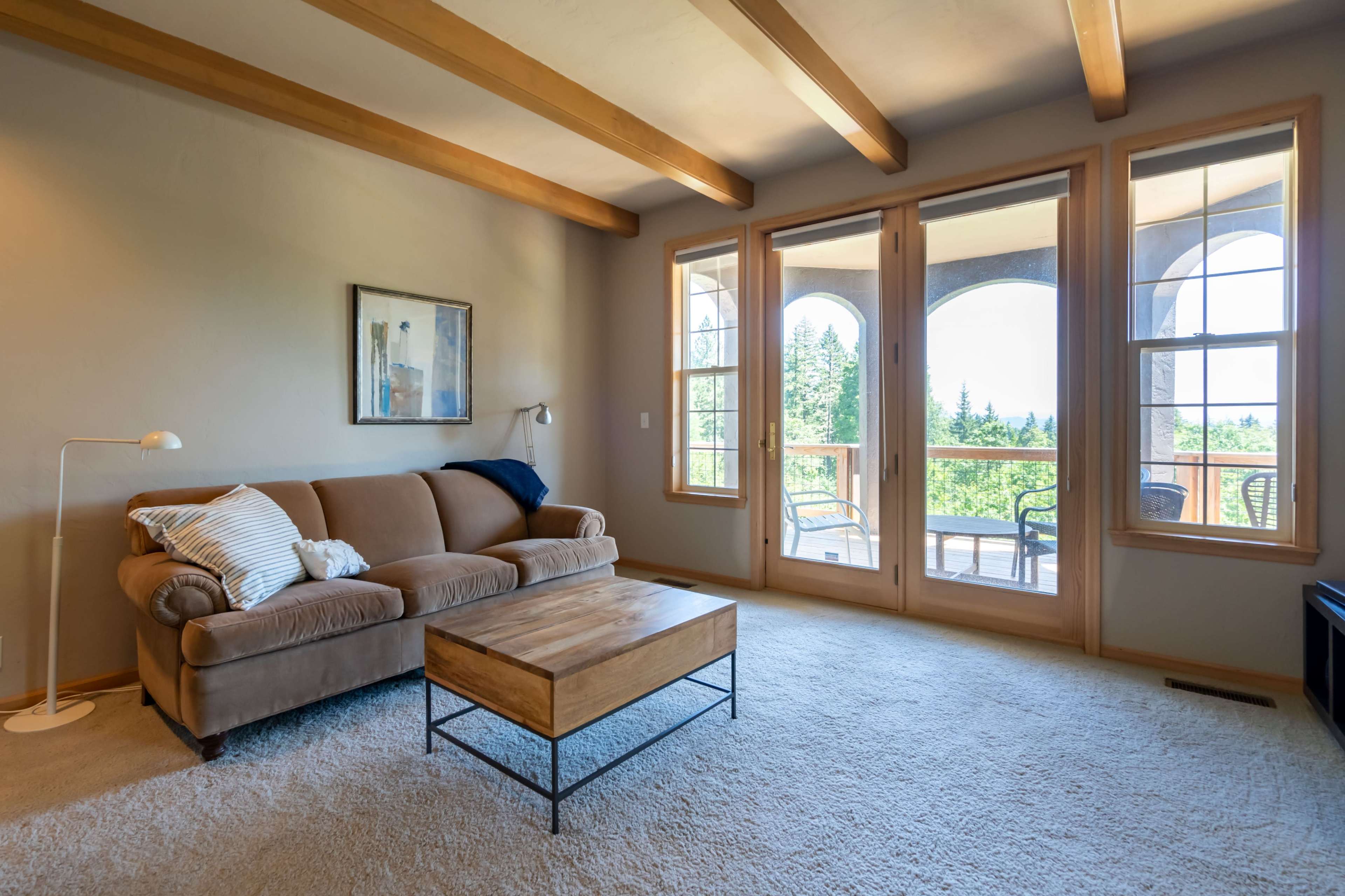 The living room features a beige sofa, a wooden coffee table, and large windows that open to a view of greenery.