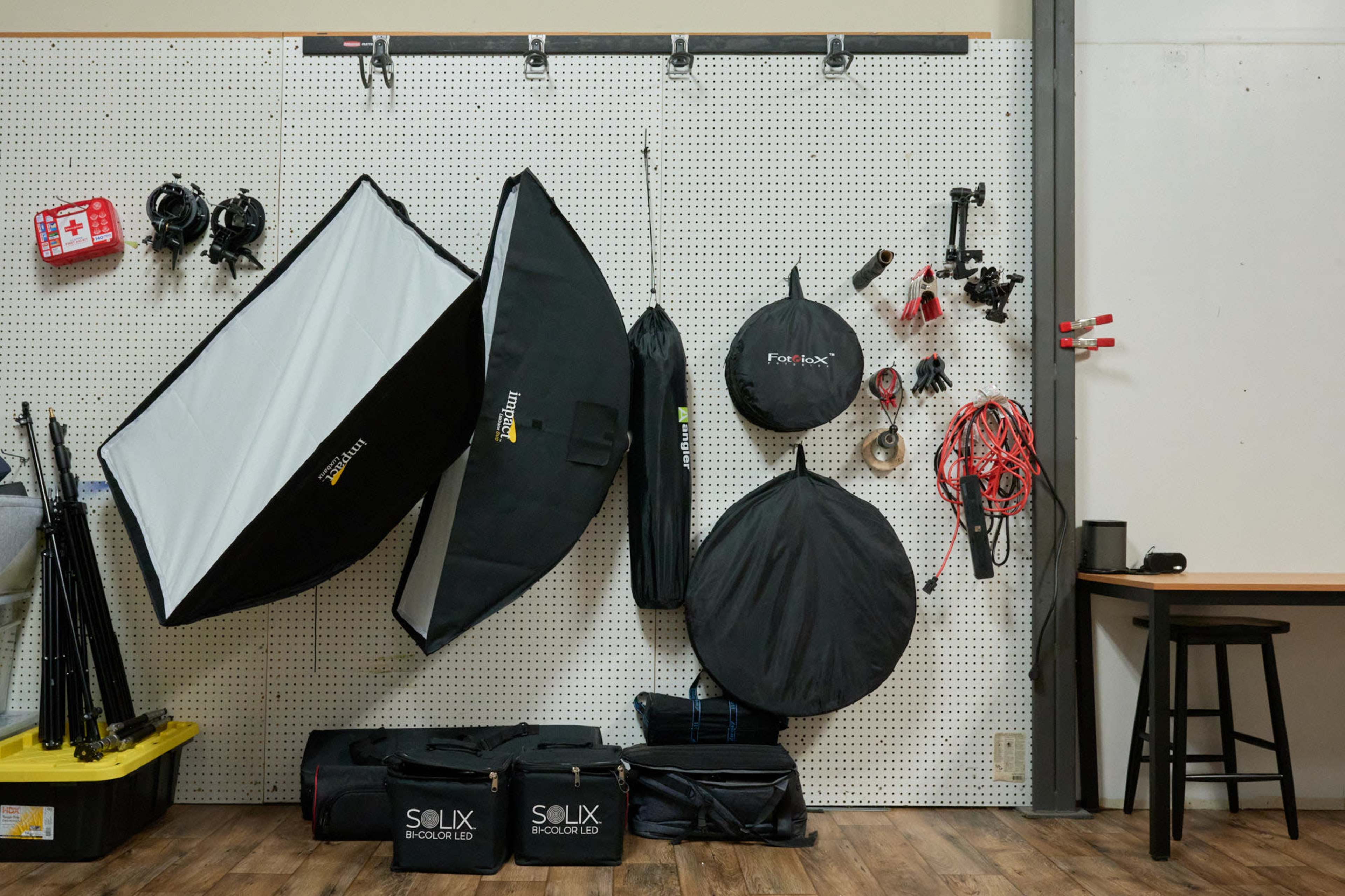 A pegboard wall with various photography equipment, including softboxes, umbrellas, and bags organized on hooks and shelves.