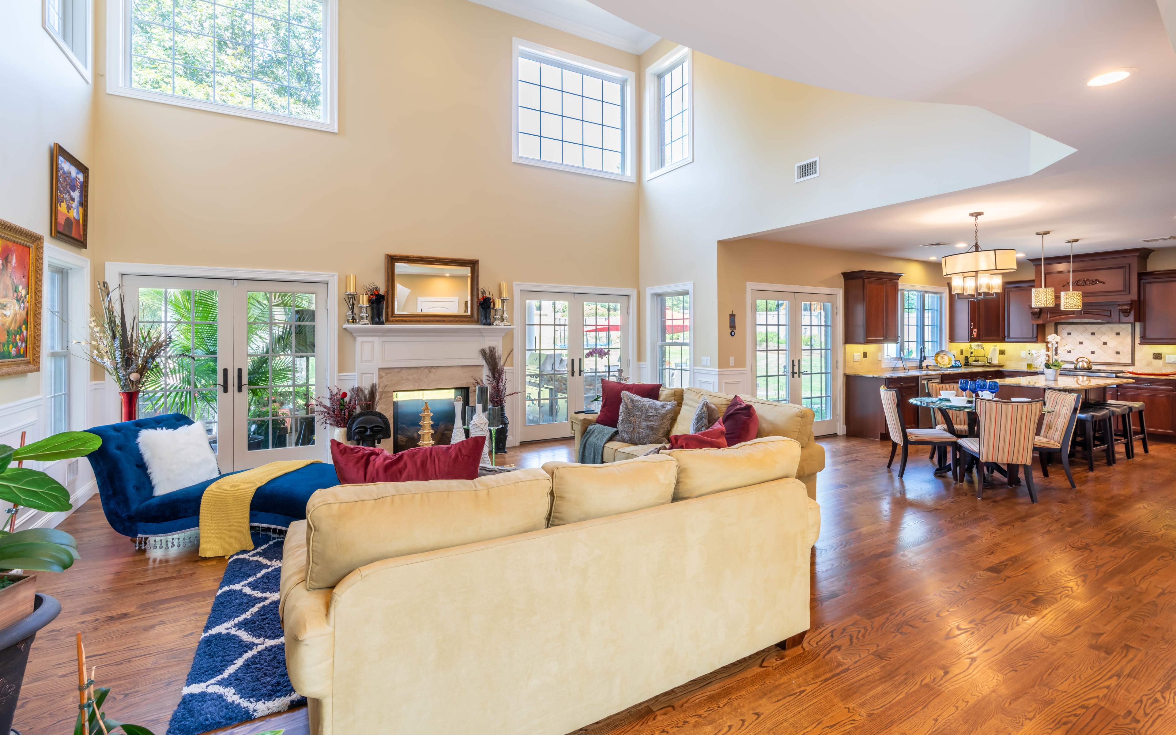 A spacious living area with a beige sofa, colorful cushions, and a modern kitchen featuring dark wood cabinetry and a dining table.