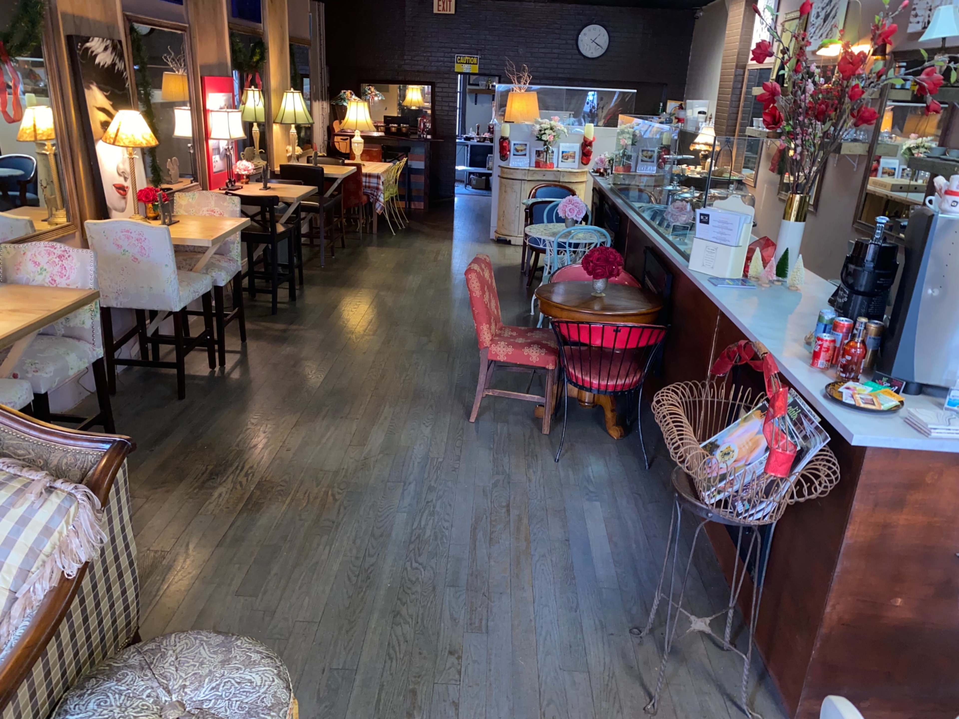 A cozy café interior with wooden floors, a mix of chairs and tables, and lamps providing ambient lighting.
