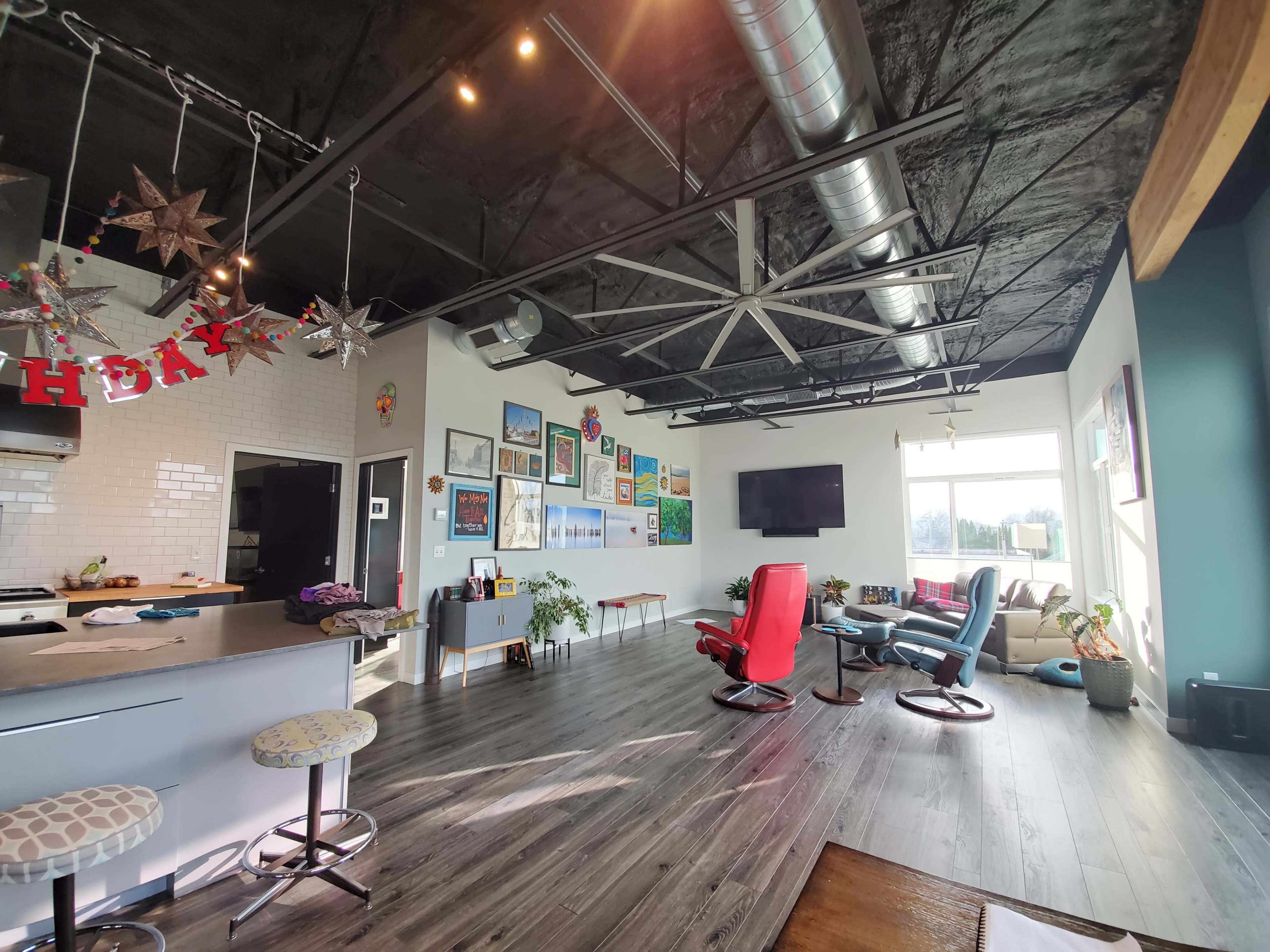 A modern open-concept living space with a kitchen area, colorful artwork on the walls, and a mix of seating options including a red recliner and a blue armchair.