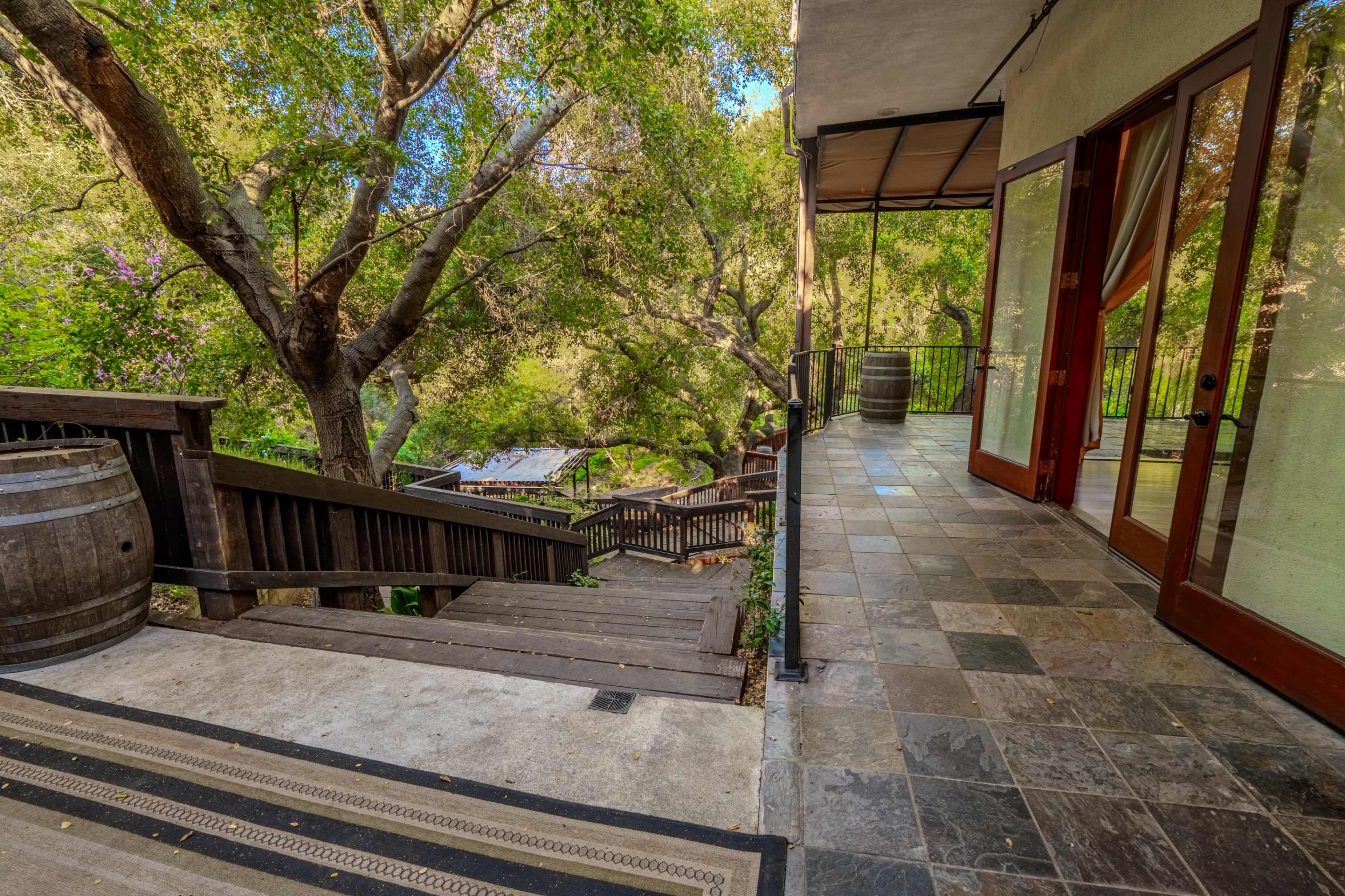 A stone pathway leads down through a lush, green landscape to a deck area, with wooden steps on one side and glass doors on the other.