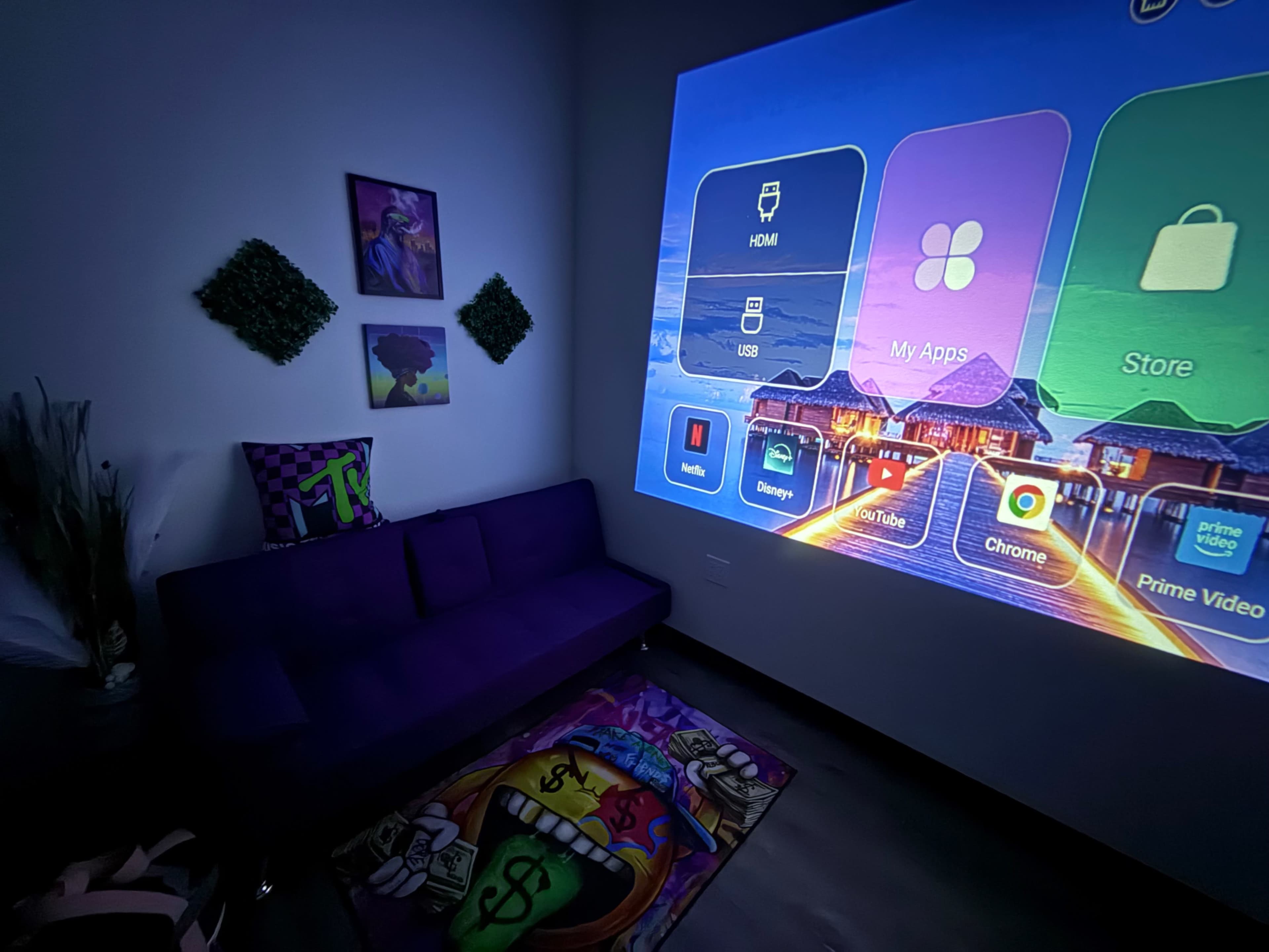 The image shows a cozy room with a purple couch and a wall displaying a large projector screen featuring various app icons.