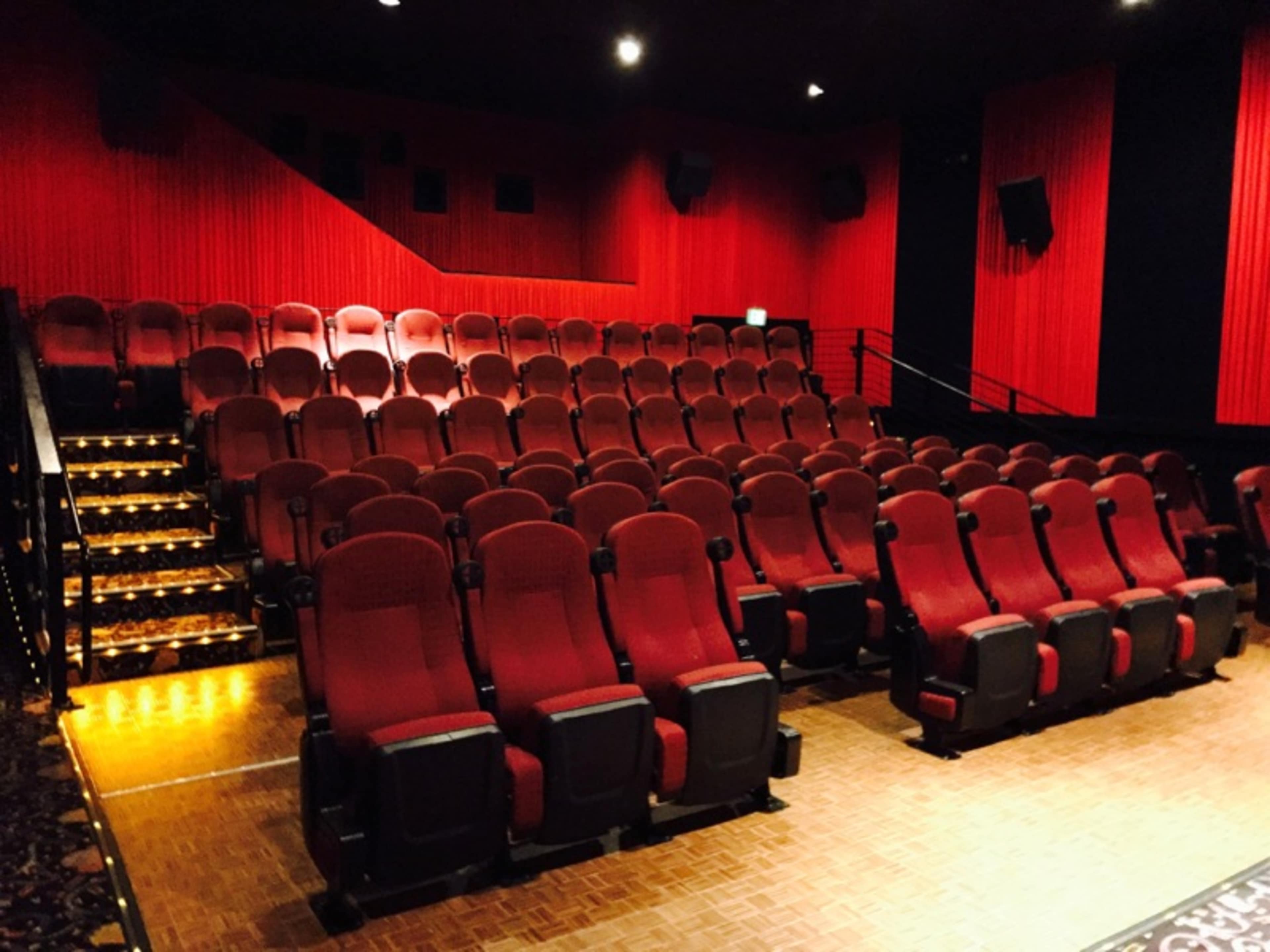 A nearly empty movie theater features rows of red upholstered seats and a red wall backdrop.