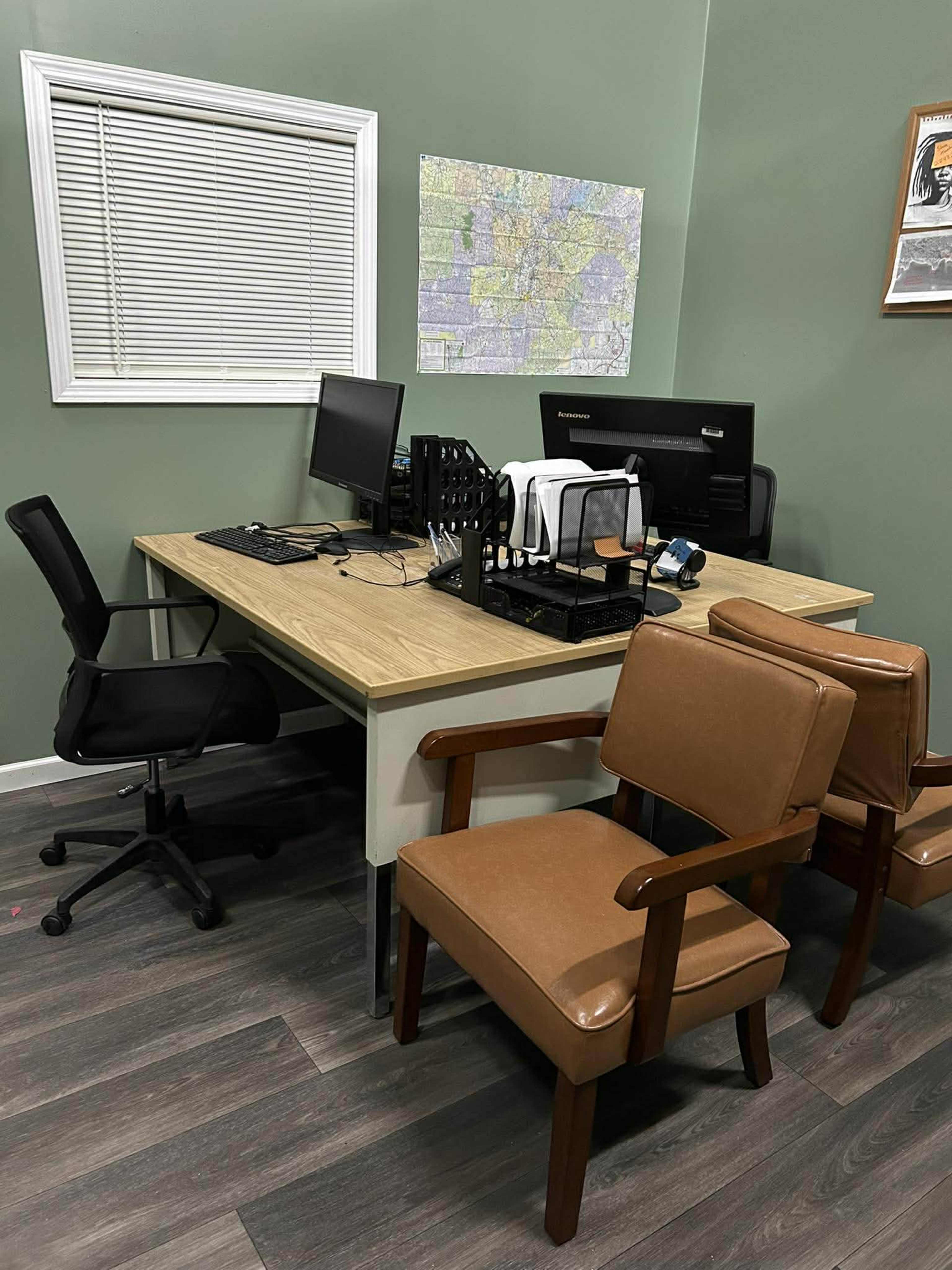 The image shows a small office space with a wooden desk, two office chairs, and a wall-mounted map.