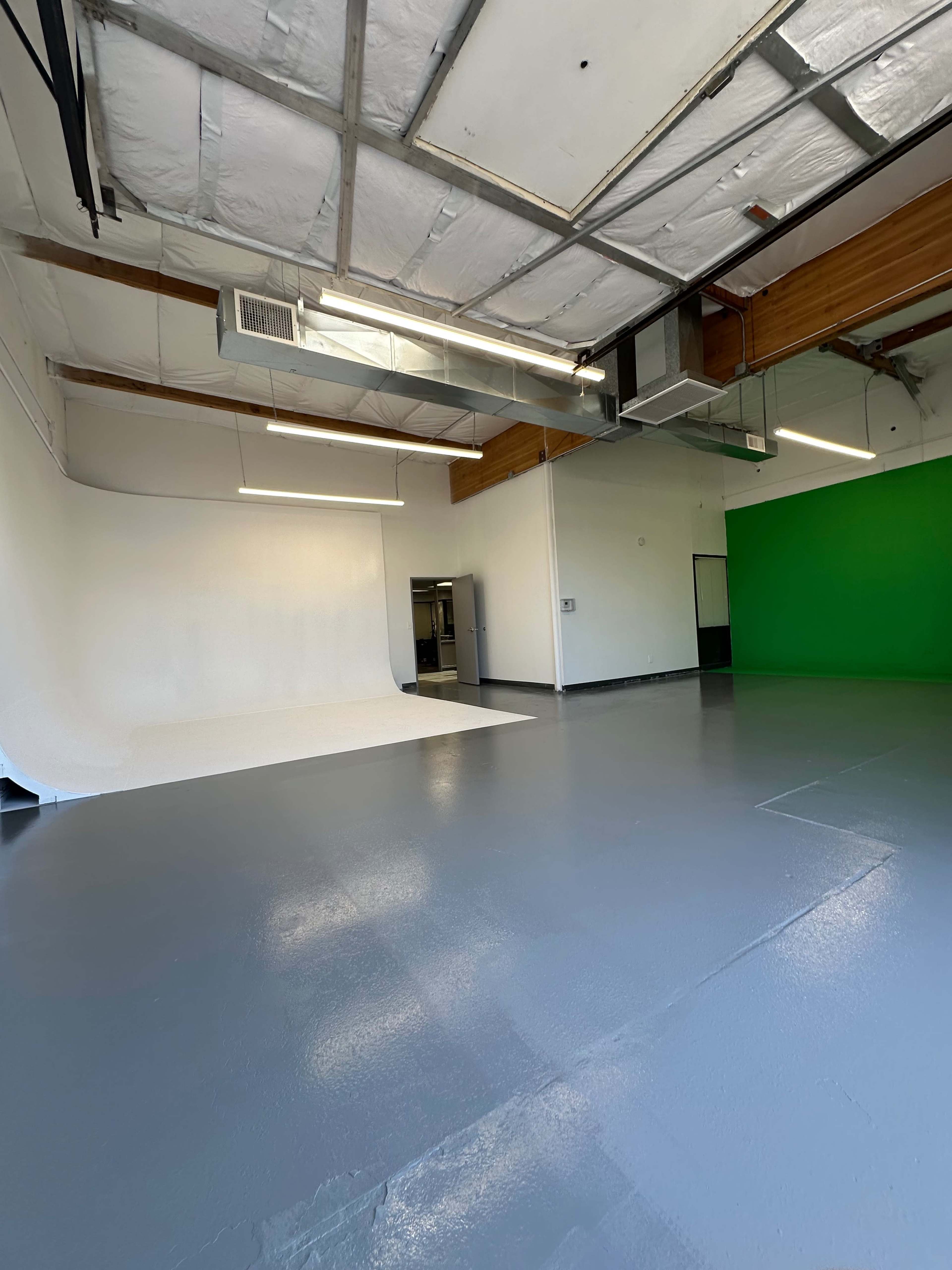 The image shows a spacious studio with a smooth gray floor, a white backdrop, and a green screen on one wall.