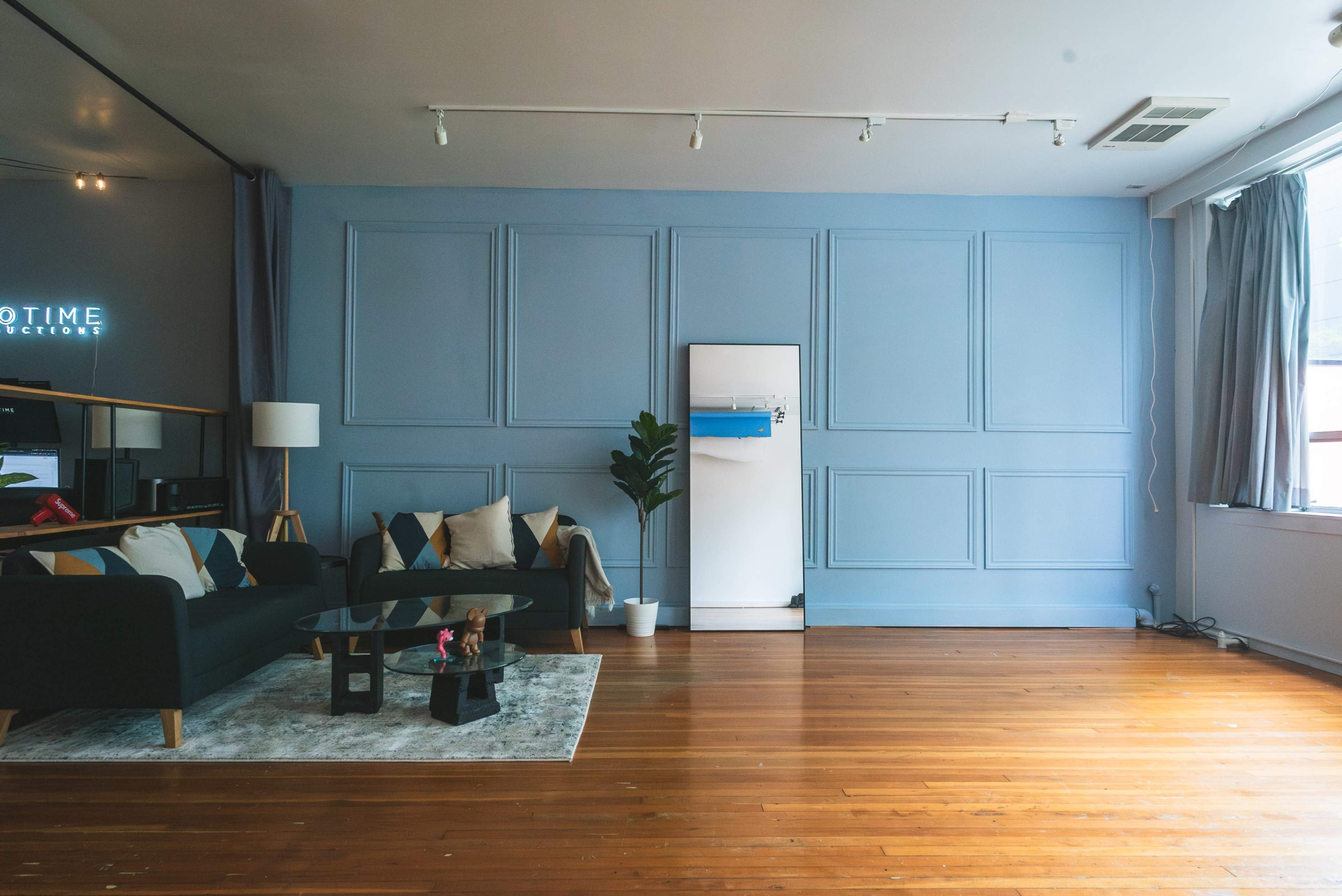 A modern living room with a blue wall, a dark green sofa, a white fridge, and a small plant next to a window.