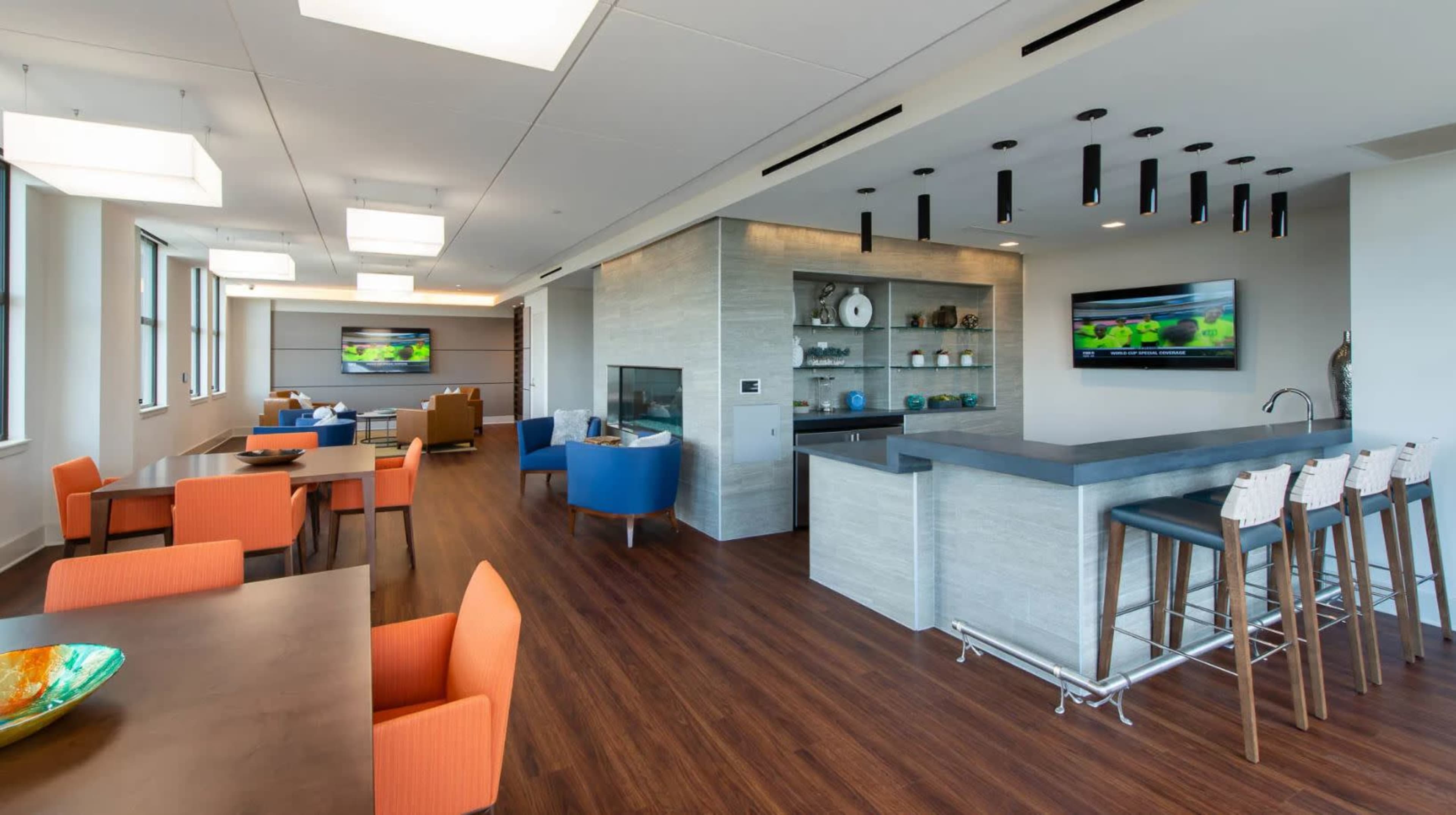 A modern lounge area with a kitchen bar, seating arrangements, and large windows providing ample natural light.