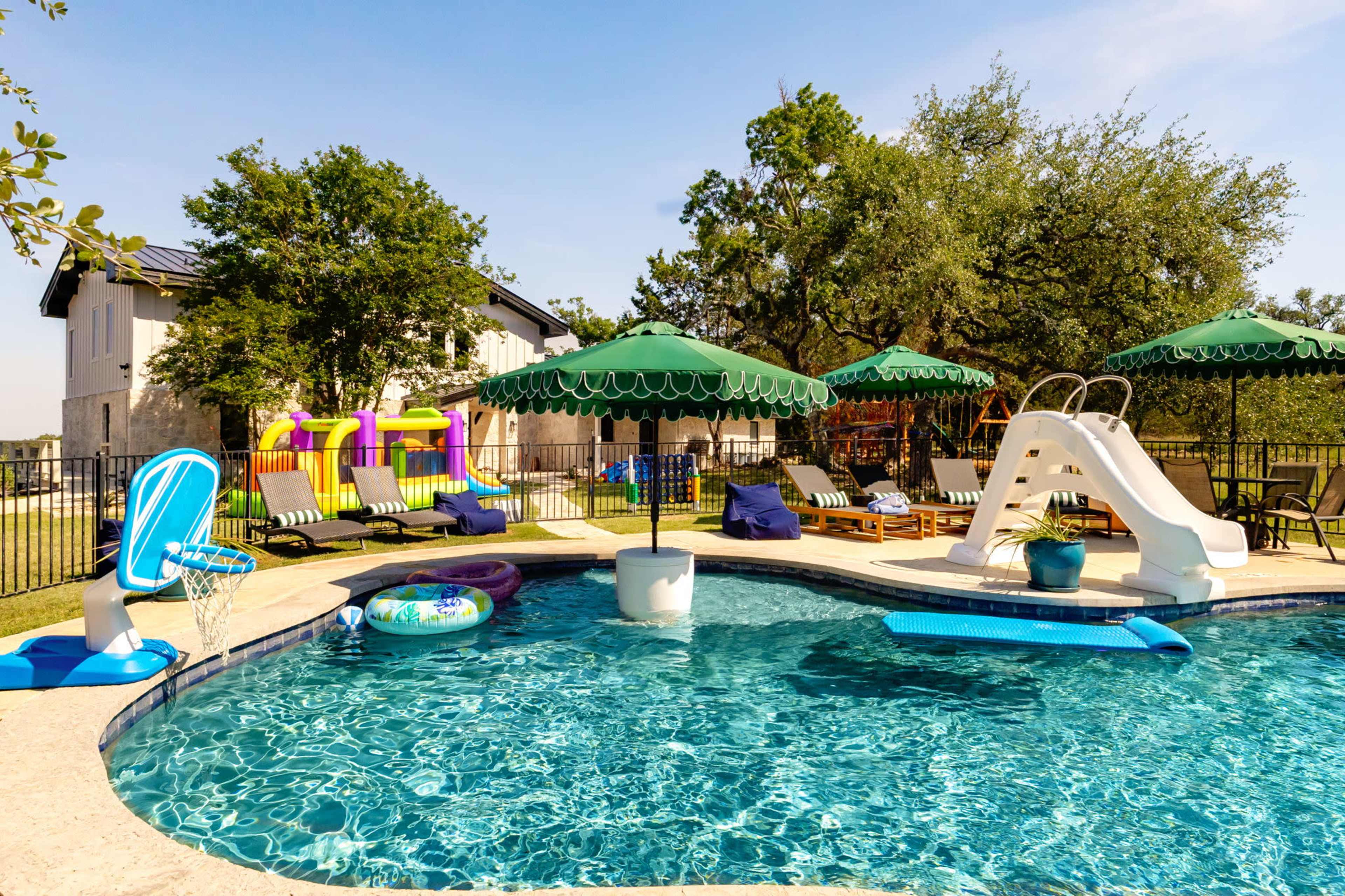 The image shows a backyard swimming pool surrounded by lounge chairs, a waterslide, and outdoor play equipment under large green umbrellas.
