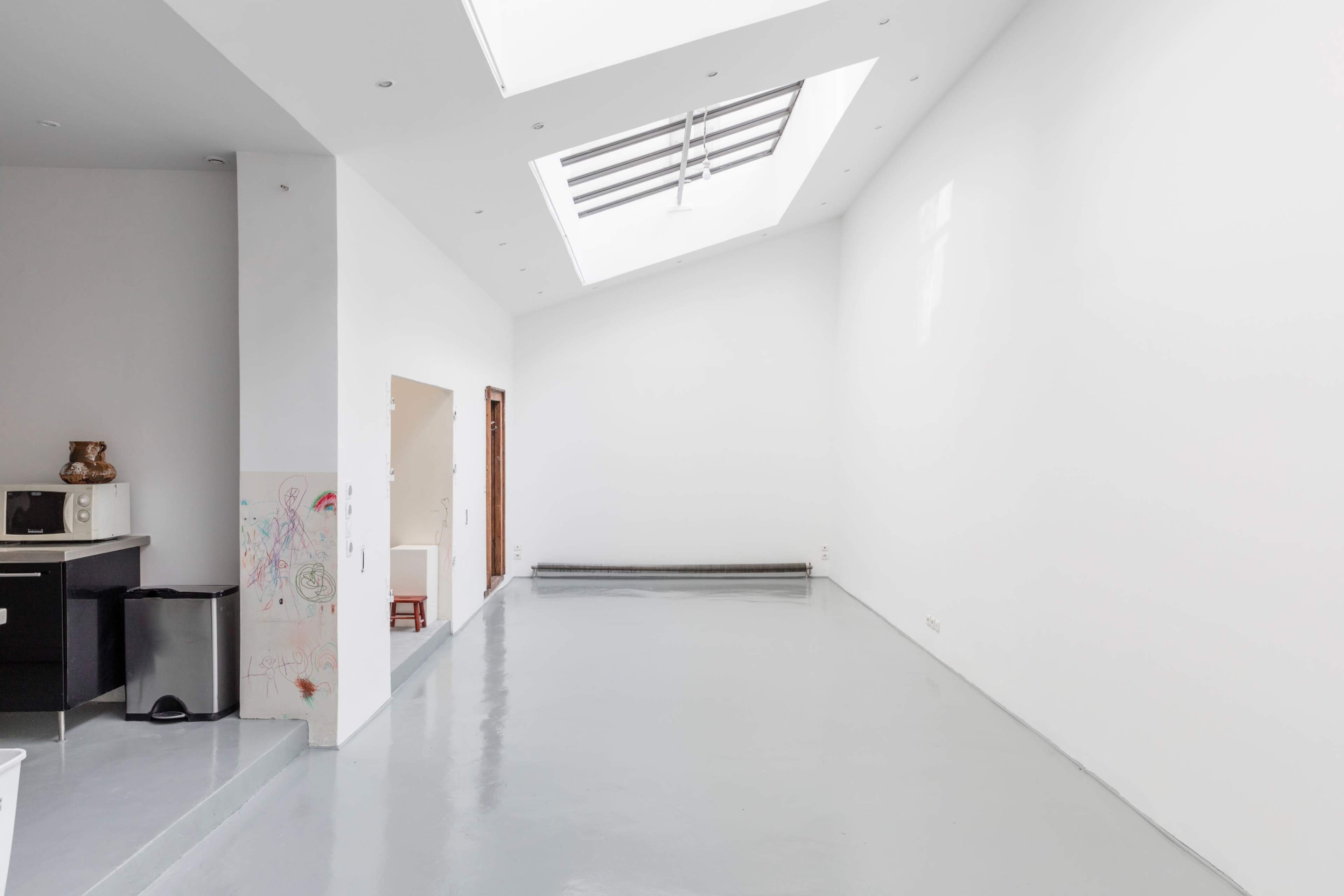 A spacious, empty room with white walls, a skylight, and a polished gray floor.