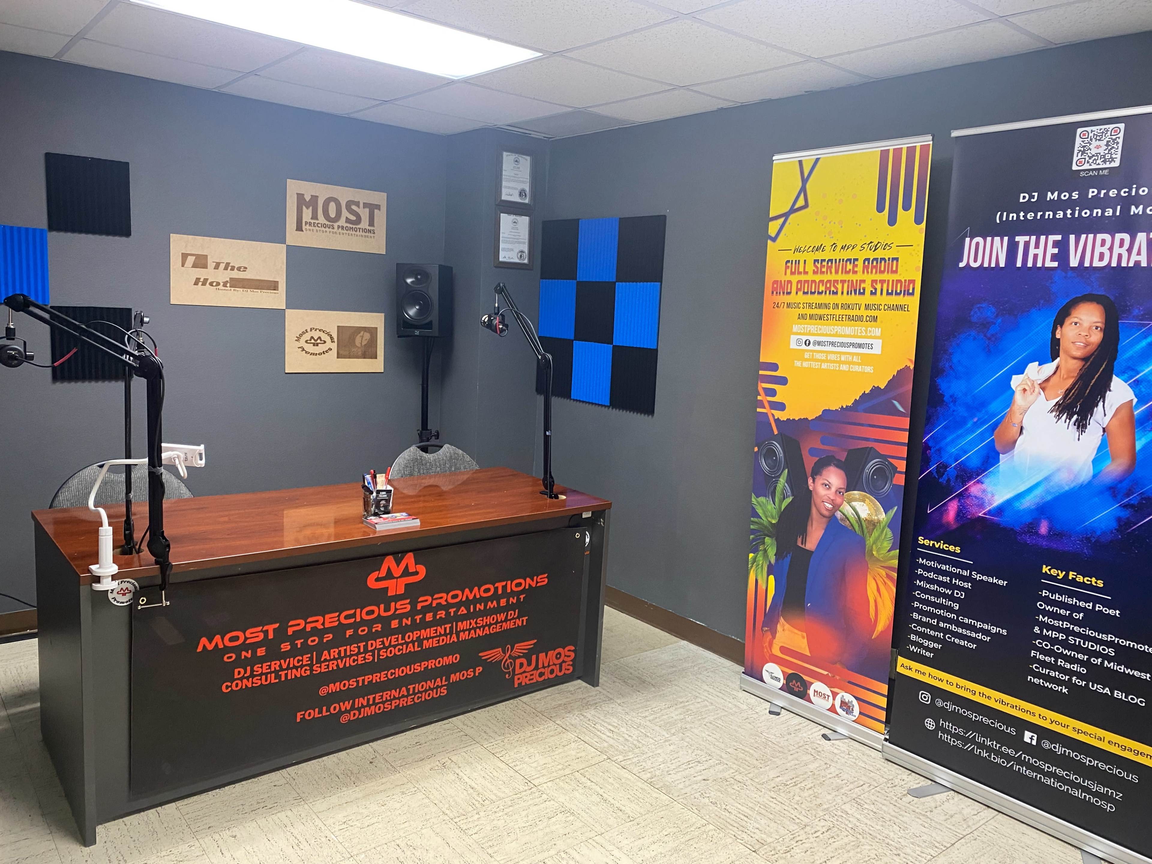 A recording studio with a desk, microphones, and promotional banners on display.