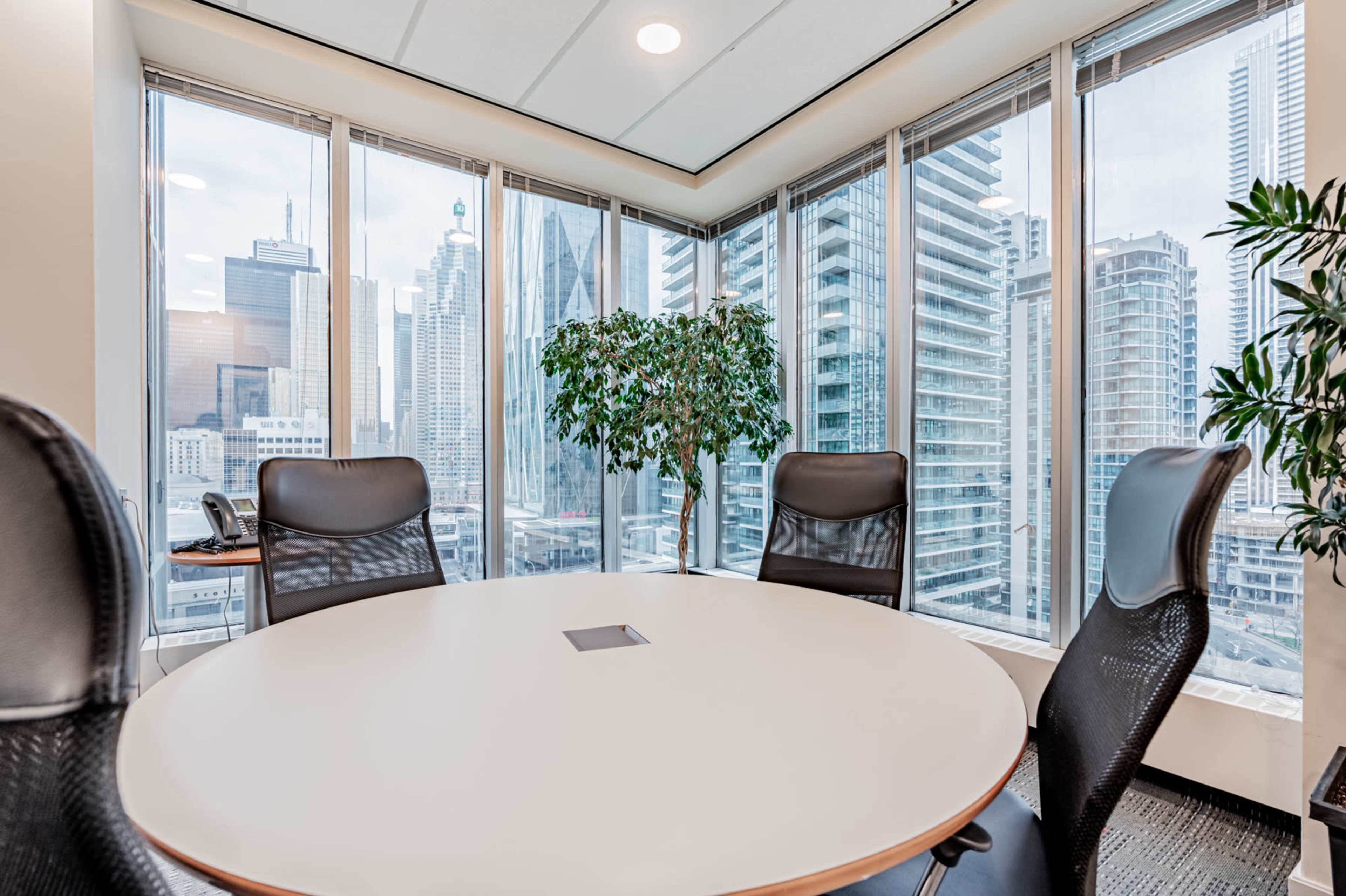 A modern conference room features a round table surrounded by black chairs, with large windows showcasing a city skyline.