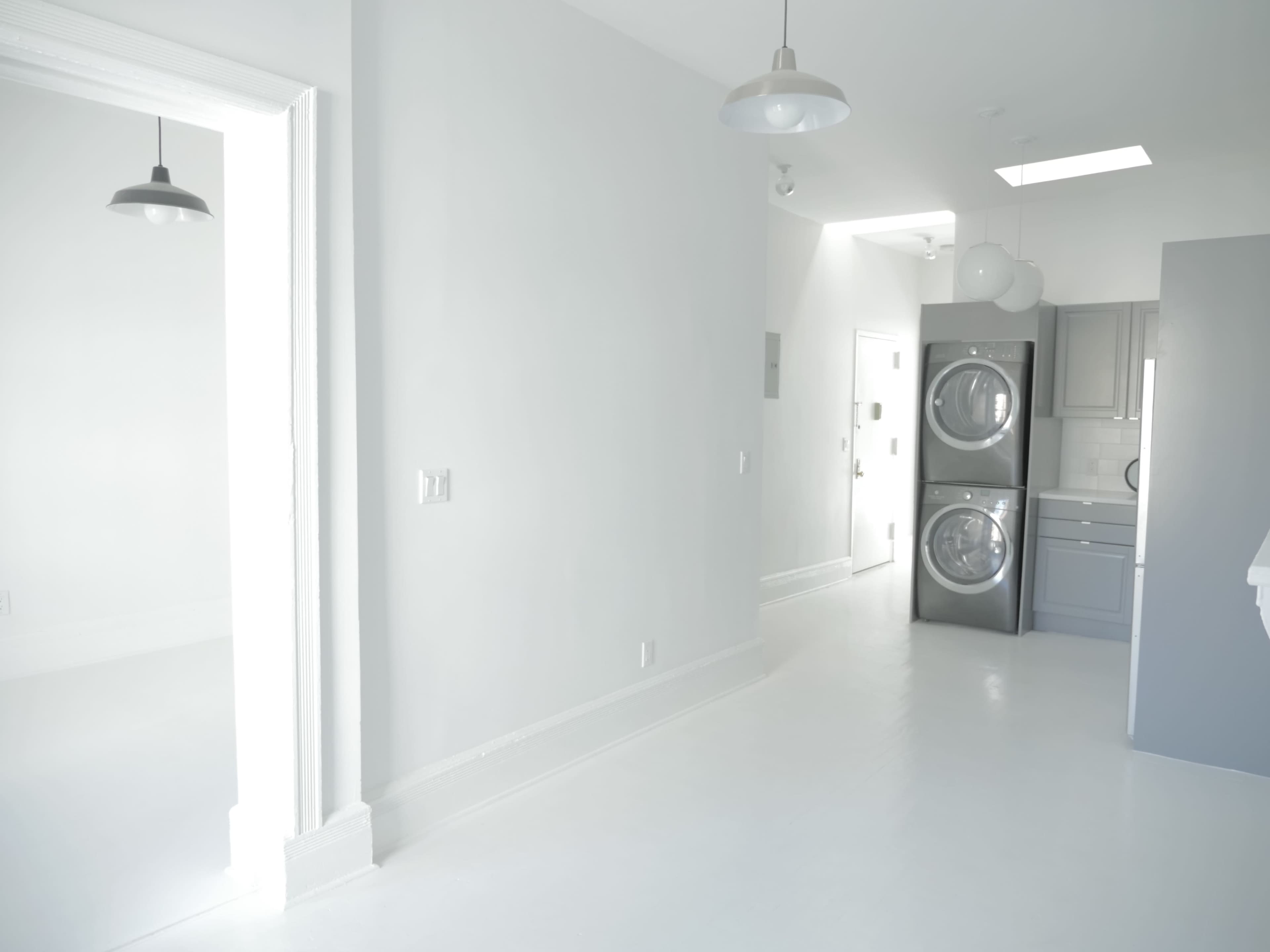 A spacious, bright interior featuring a laundry area with stacked washers and dryers on the right and a doorway leading to another room on the left.