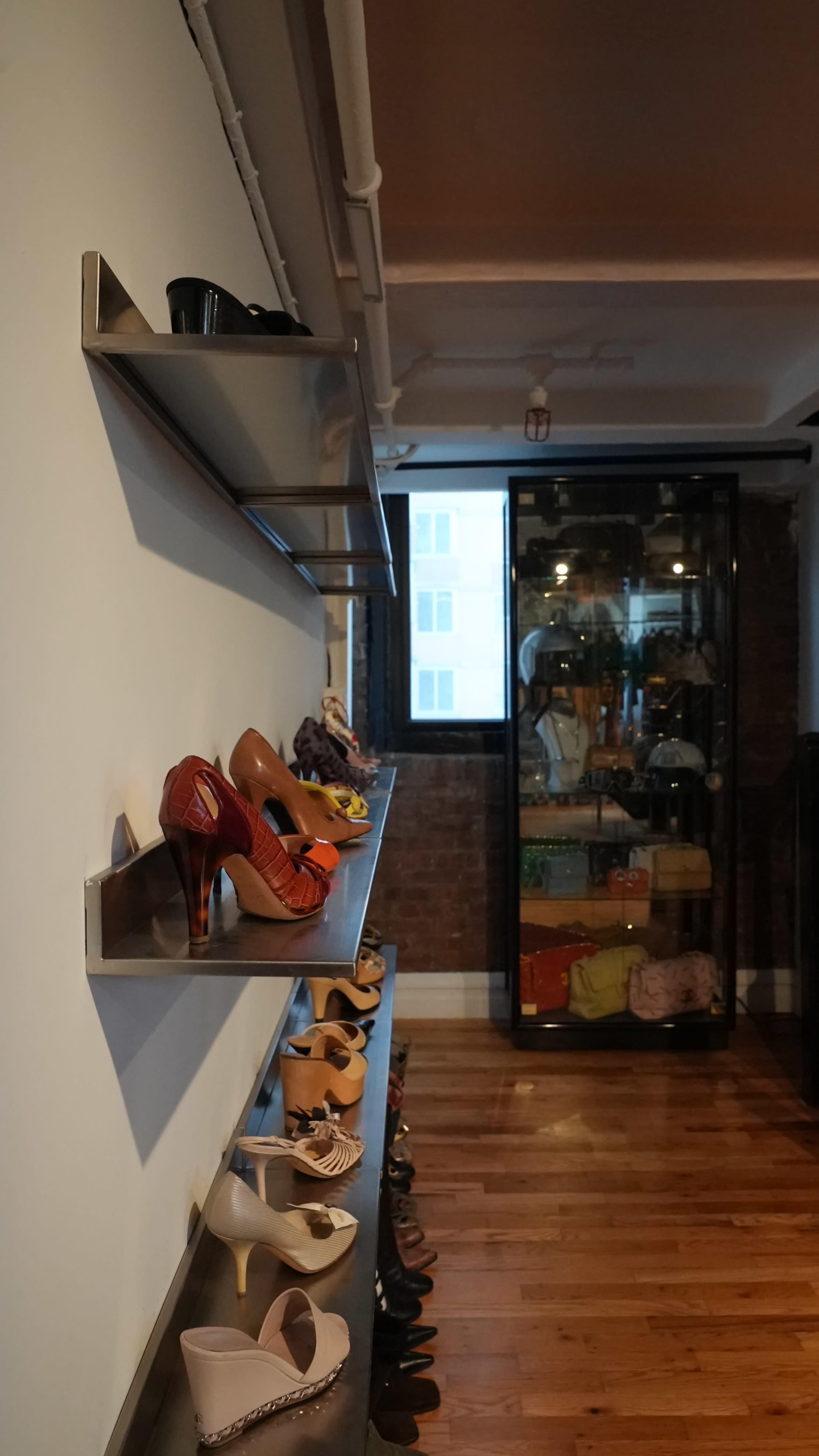 The image shows a boutique interior with a wall-mounted shelf displaying various pairs of shoes, and a glass display cabinet filled with bags and accessories.