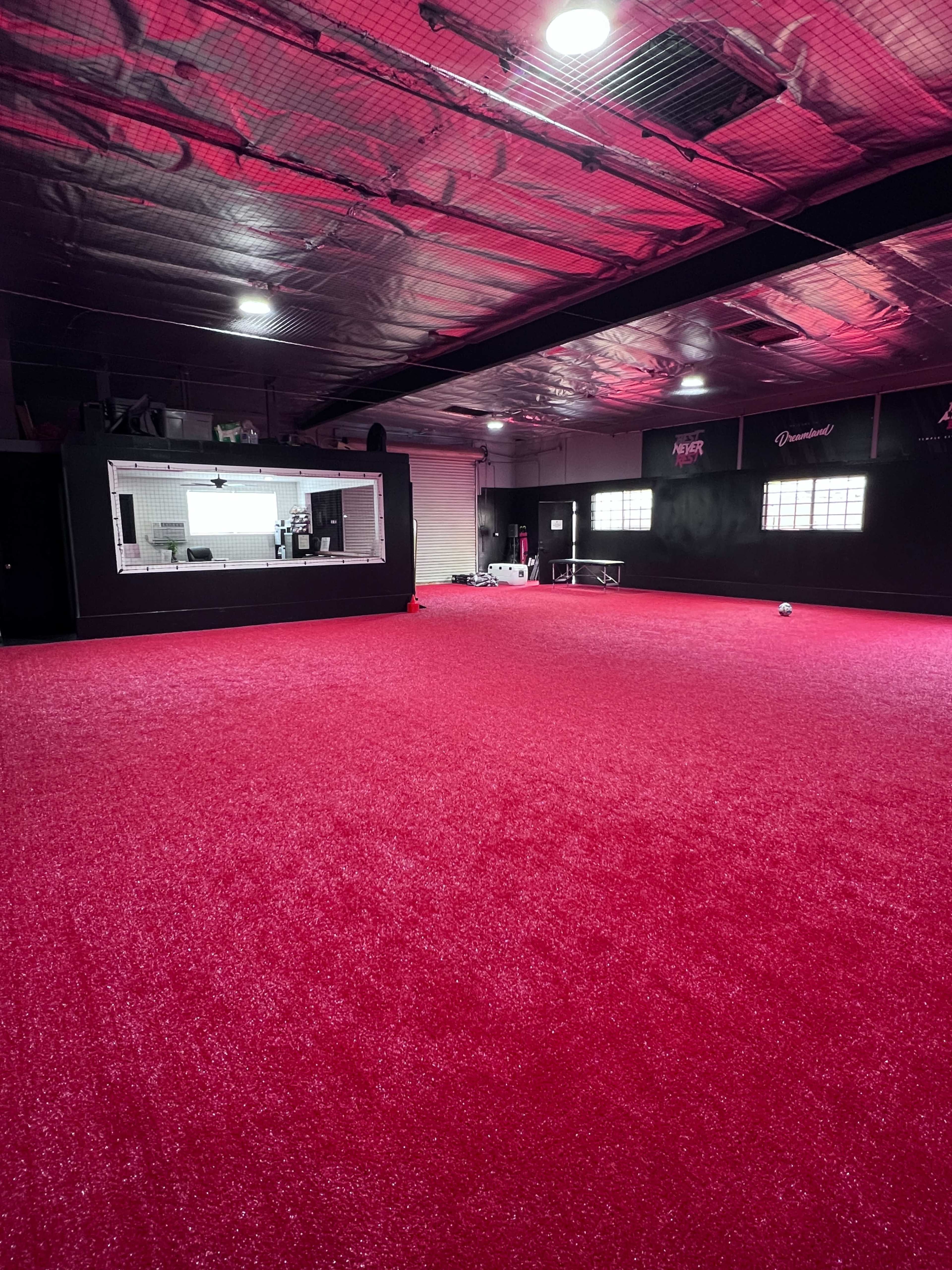 The image shows an indoor facility with bright pink carpet flooring and a large window looking into a separate room.