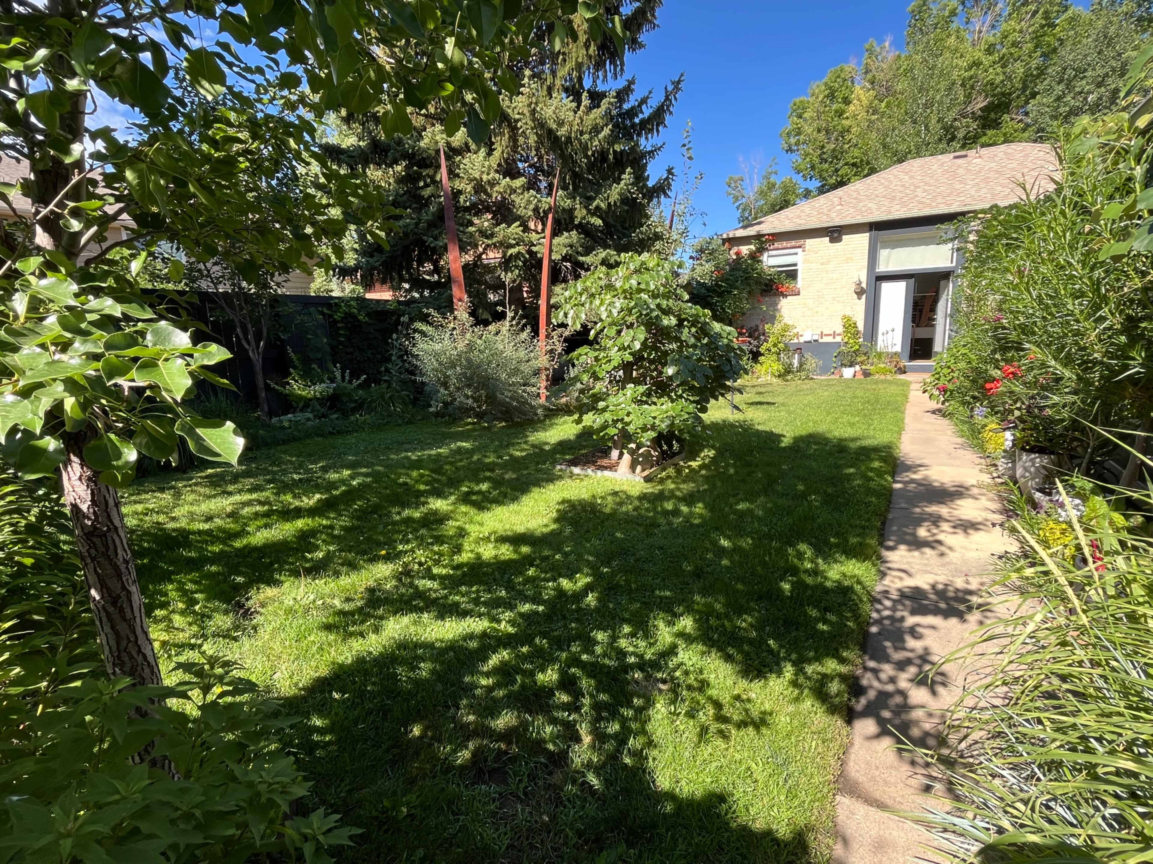 The image shows a well-kept garden with a manicured lawn, trees, and a pathway leading to a house in the background.