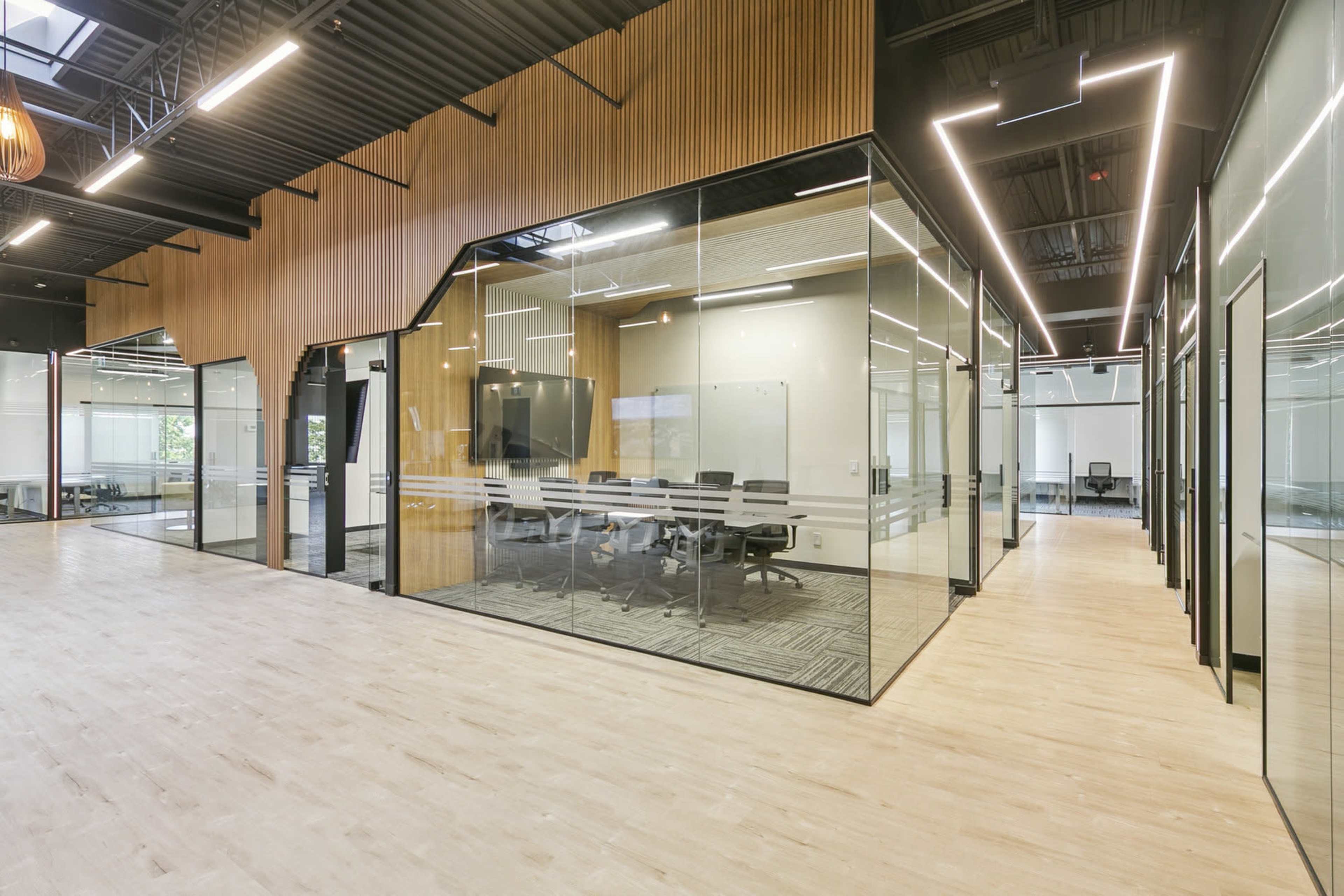 The image depicts a modern office space featuring glass-walled meeting rooms with wooden accents and a large open area with wooden flooring.