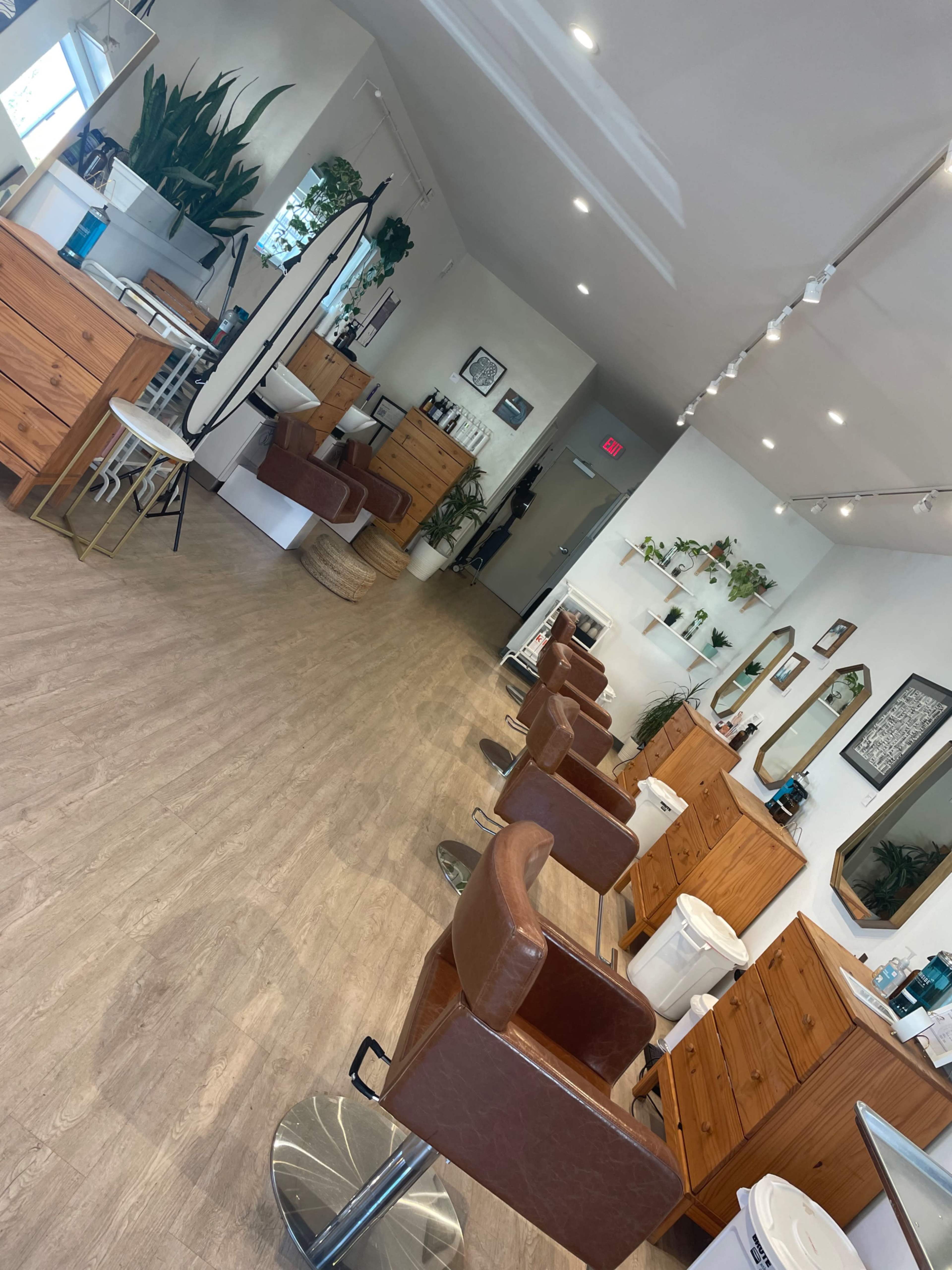 A spacious hair salon with wooden furniture, several styling stations, and a seating area.