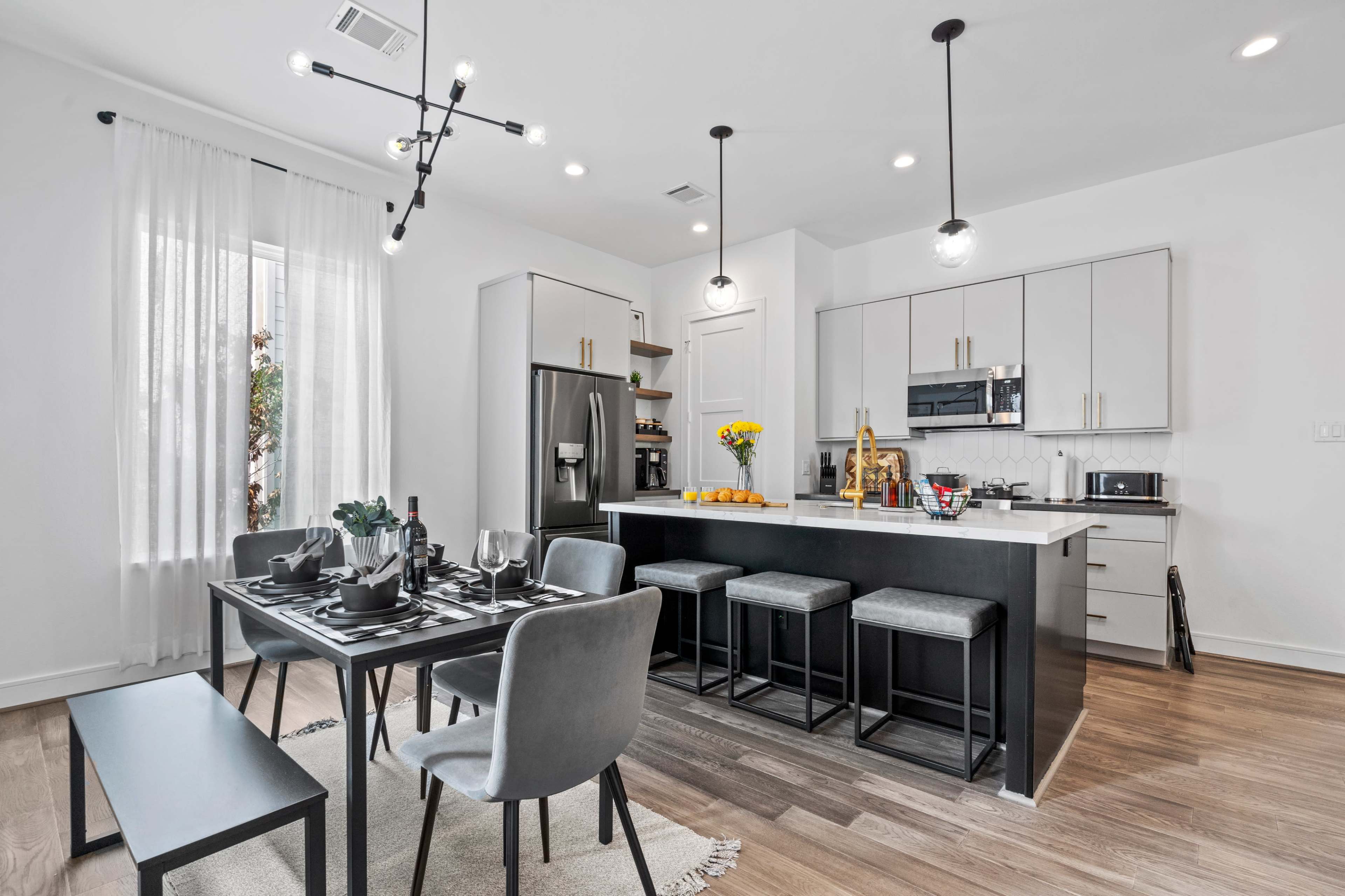 A modern kitchen and dining area feature sleek cabinetry, a central island with bar stools, and a dining table set for four.
