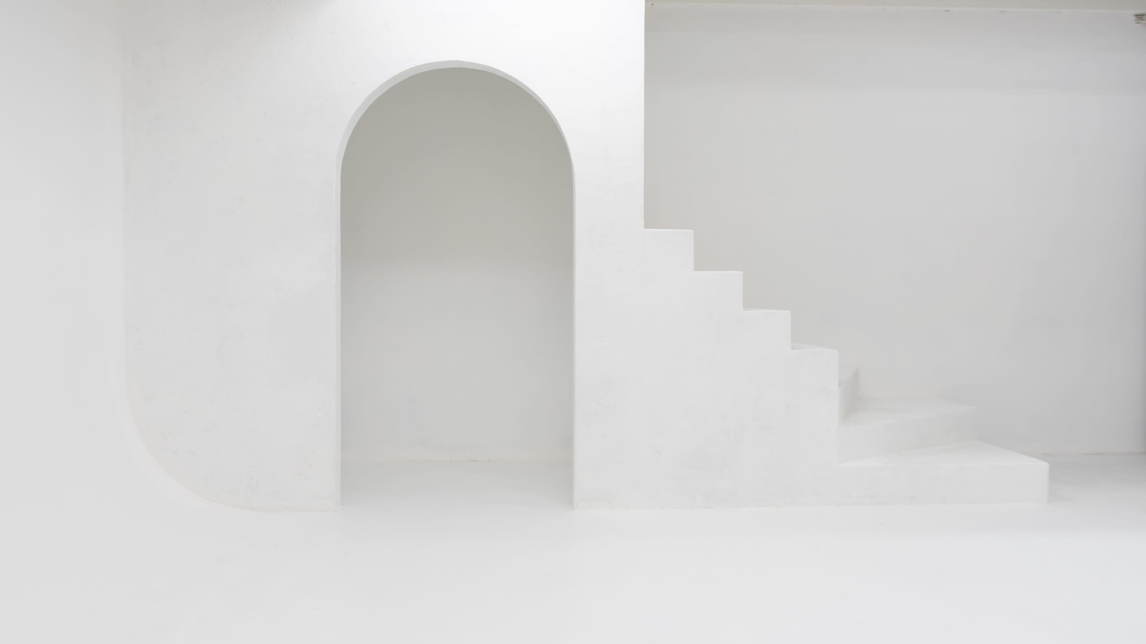 The image shows a minimalist interior featuring a curved archway and a set of white stairs against a plain white background.