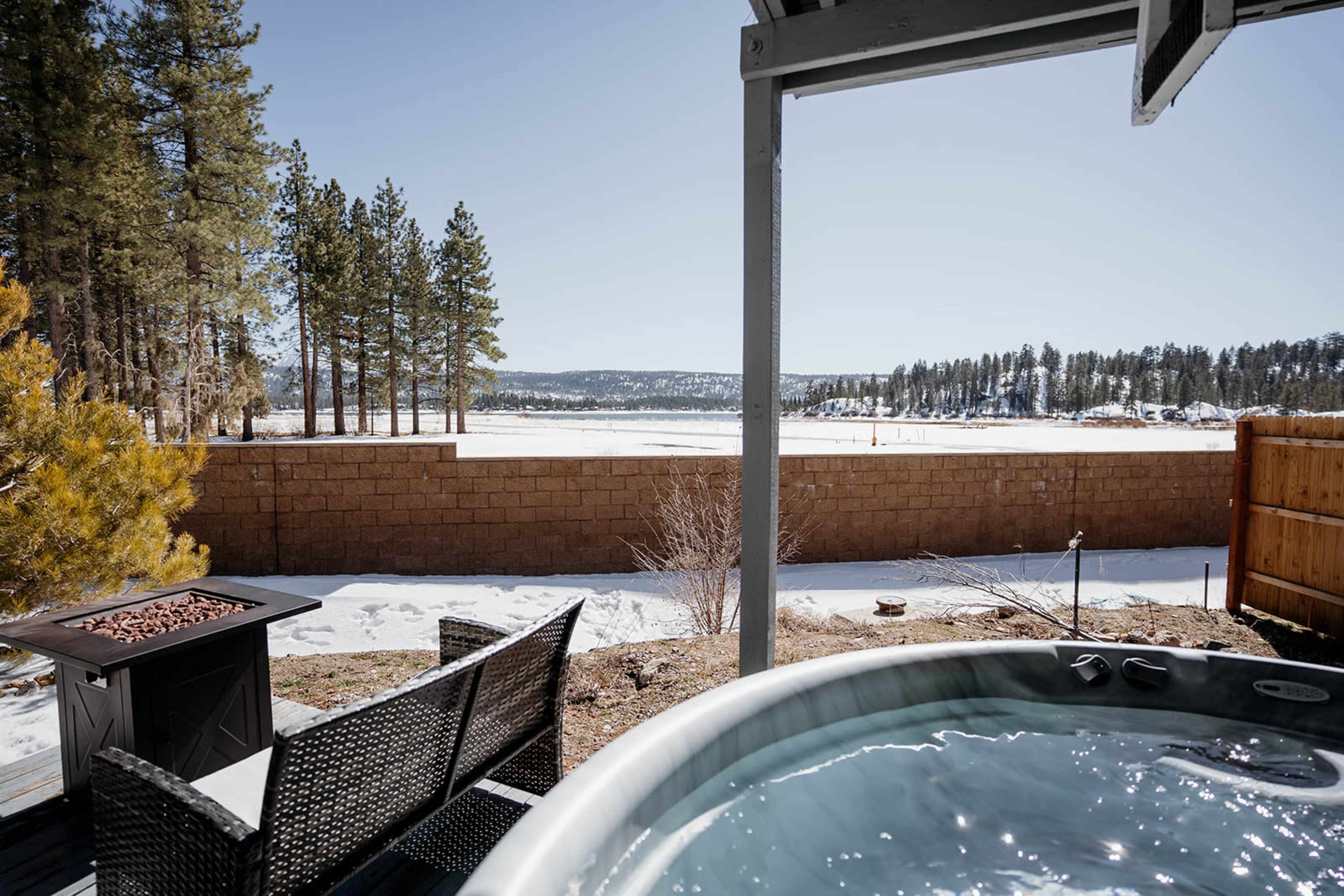 A hot tub overlooks a snowy landscape with a lake and trees in the background.