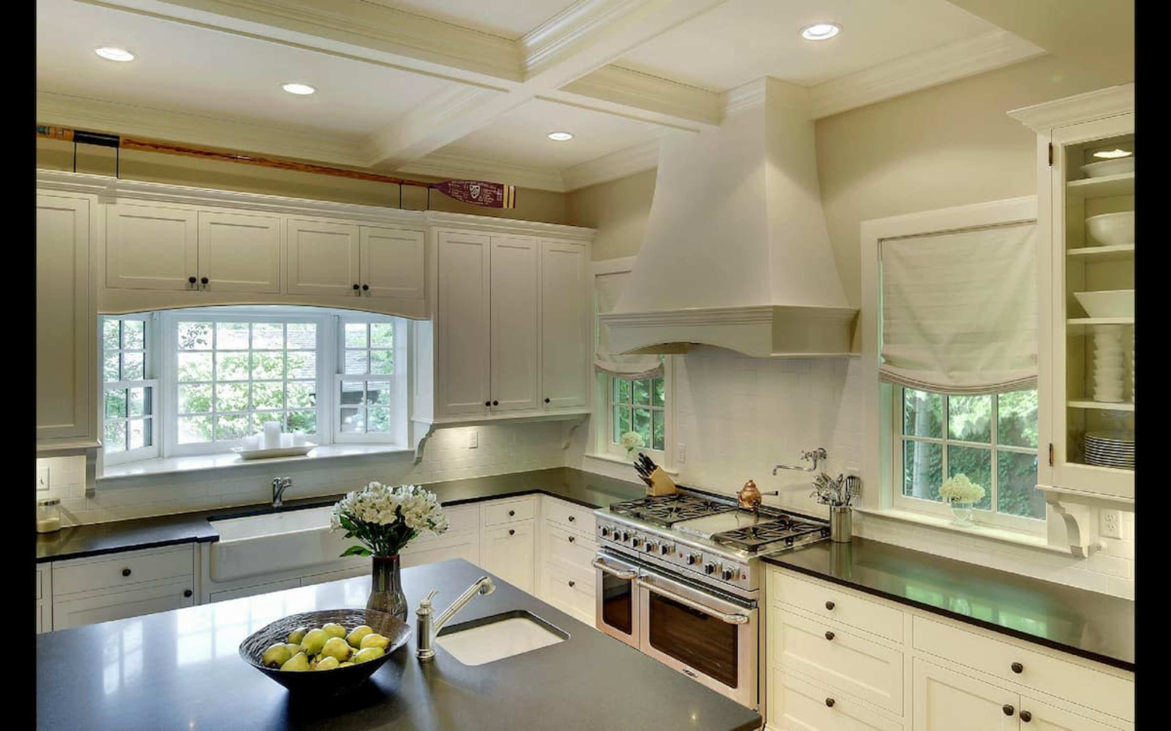 A modern kitchen features white cabinetry, a center island with a bowl of lemons, and a large window overlooking greenery.