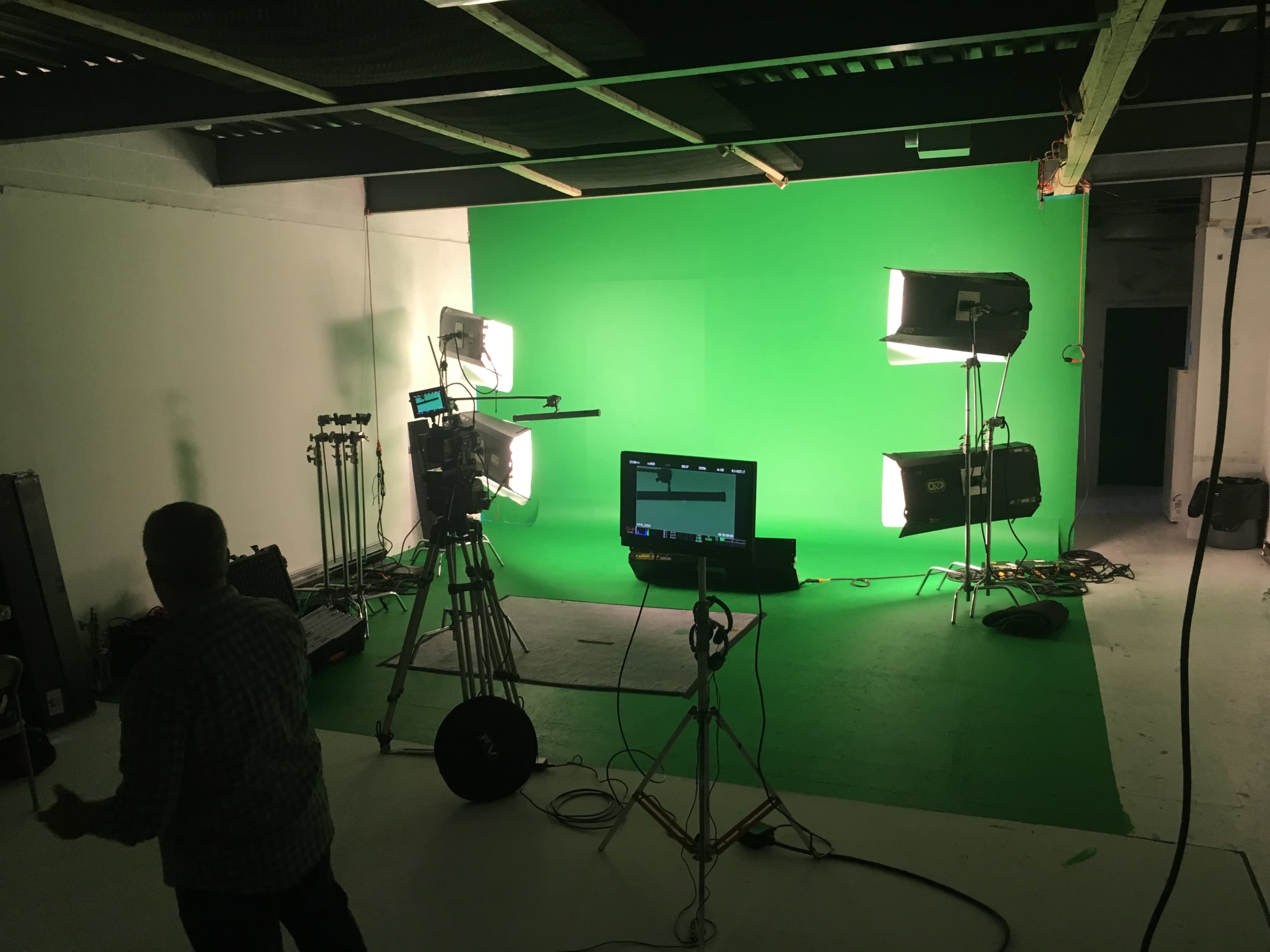 A film studio features a green screen setup with bright lights and a camera on a tripod.