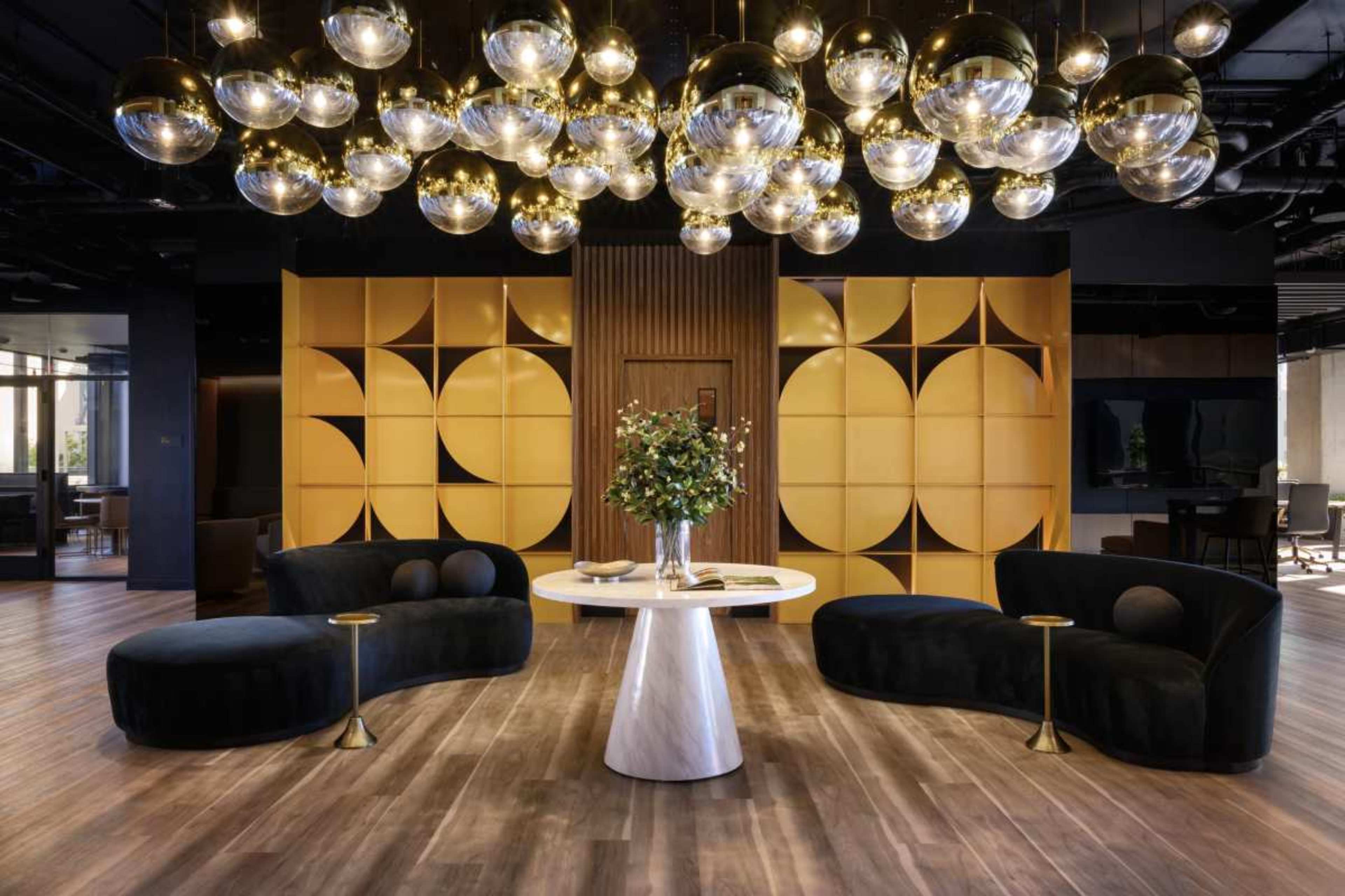 A modern lobby features circular pendant lights overhead, a round table at the center, and two curved sofas placed on either side.