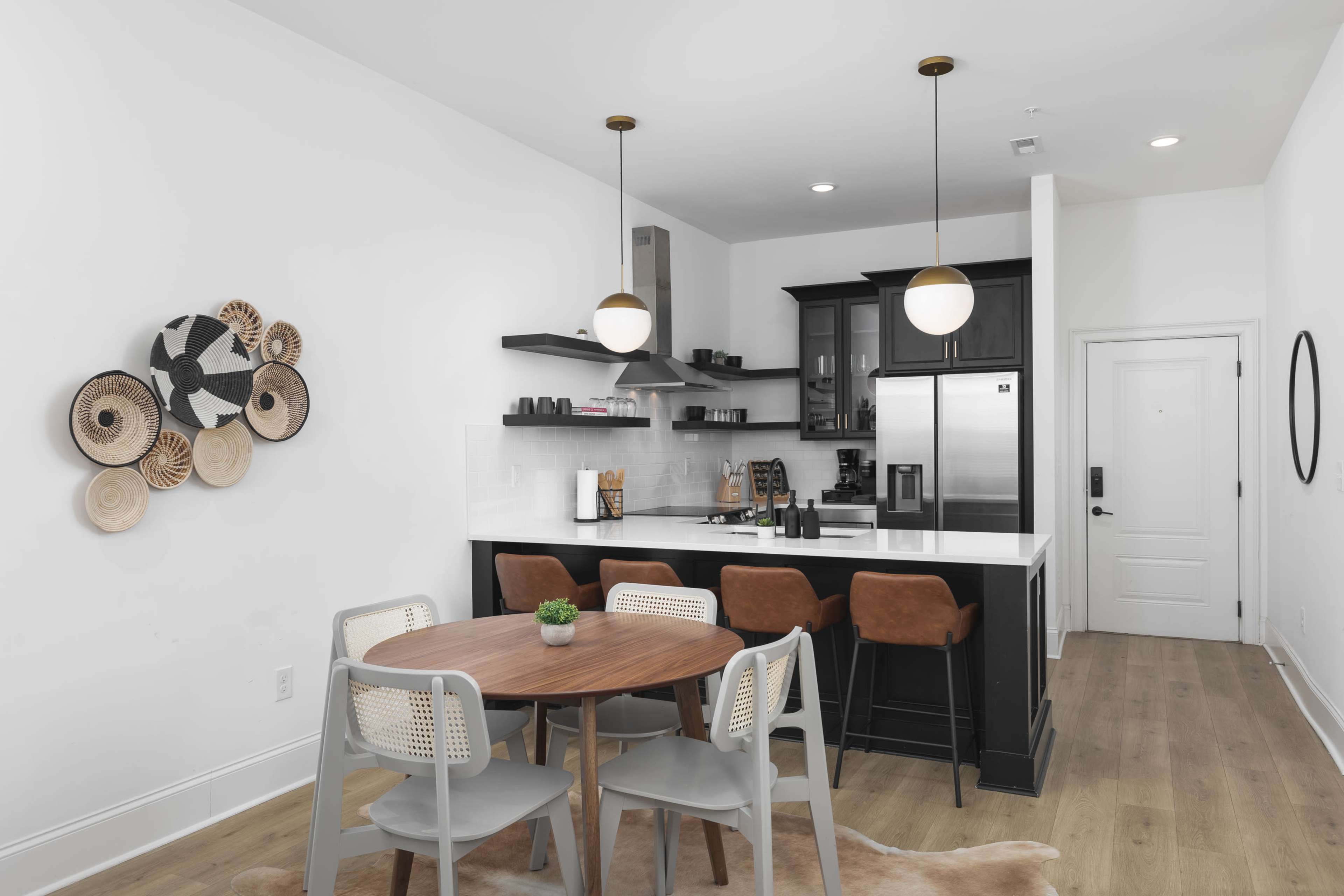 A modern kitchen with black cabinets and stainless steel appliances is connected to a dining area featuring a round wooden table and gray chairs.
