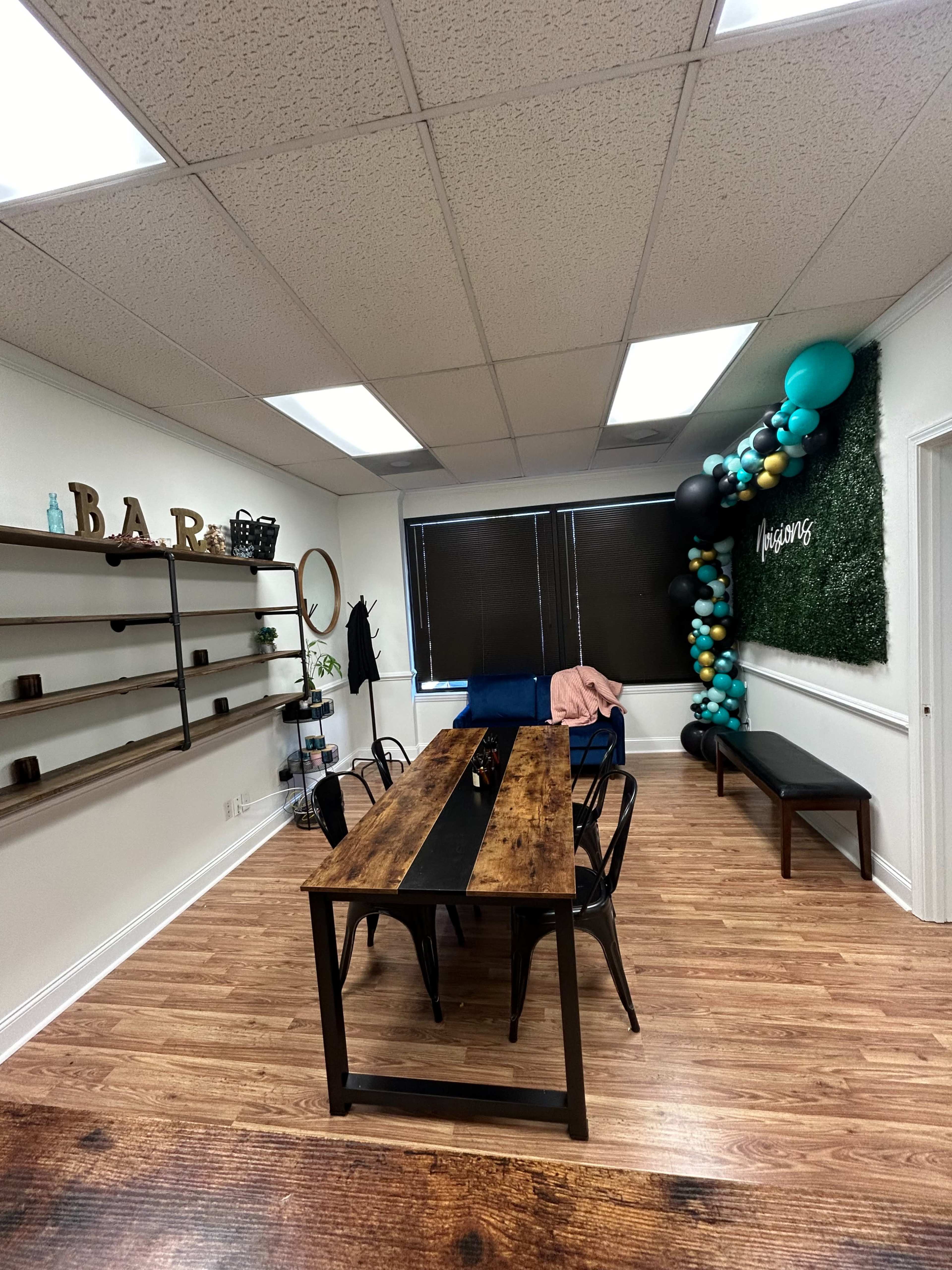 A modern office space featuring a wooden dining table, black chairs, decorative shelves, and a green wall adorned with balloons.